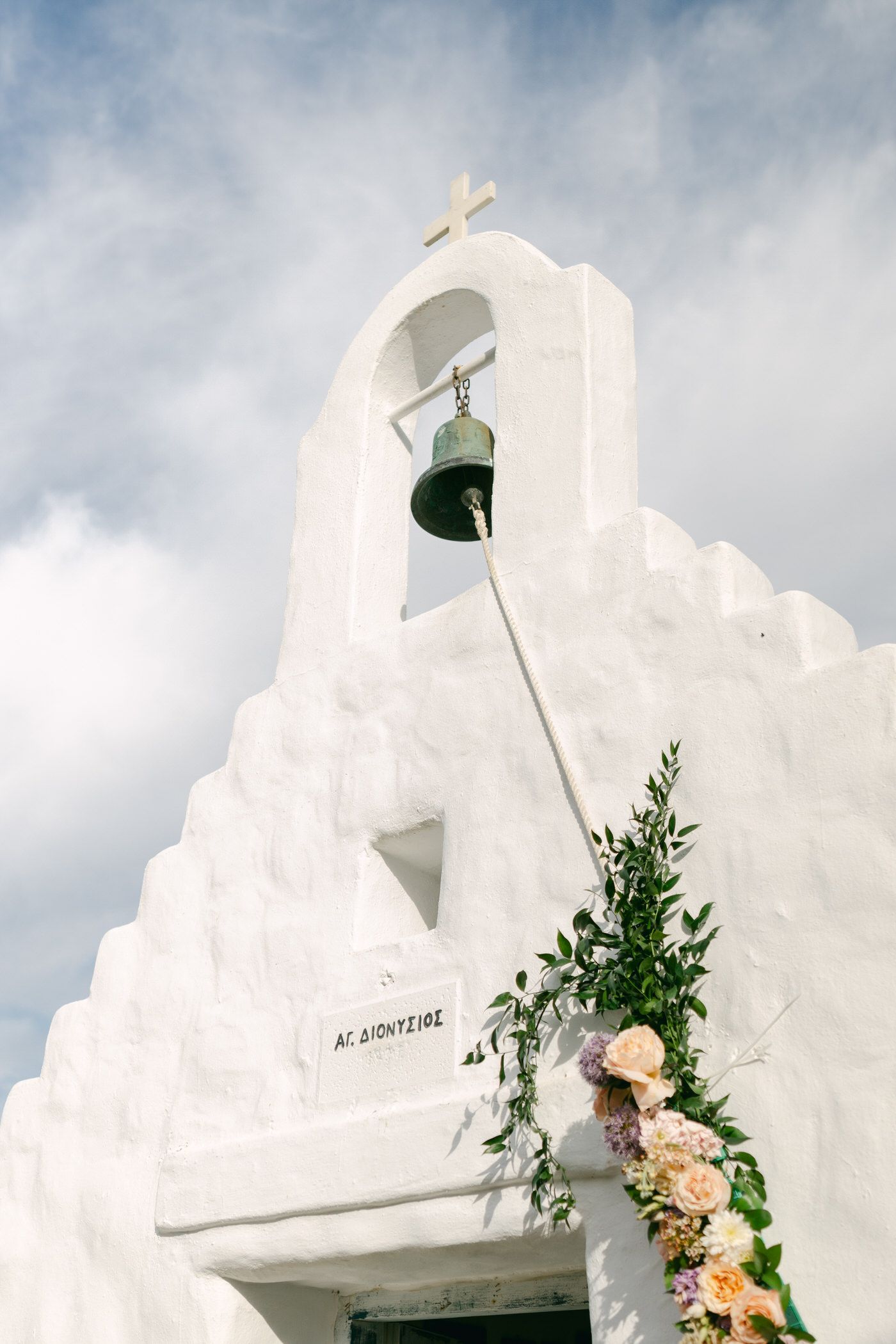 White church bell tower with peach flowers and greenery decorating its entrance against a cloudy sky.