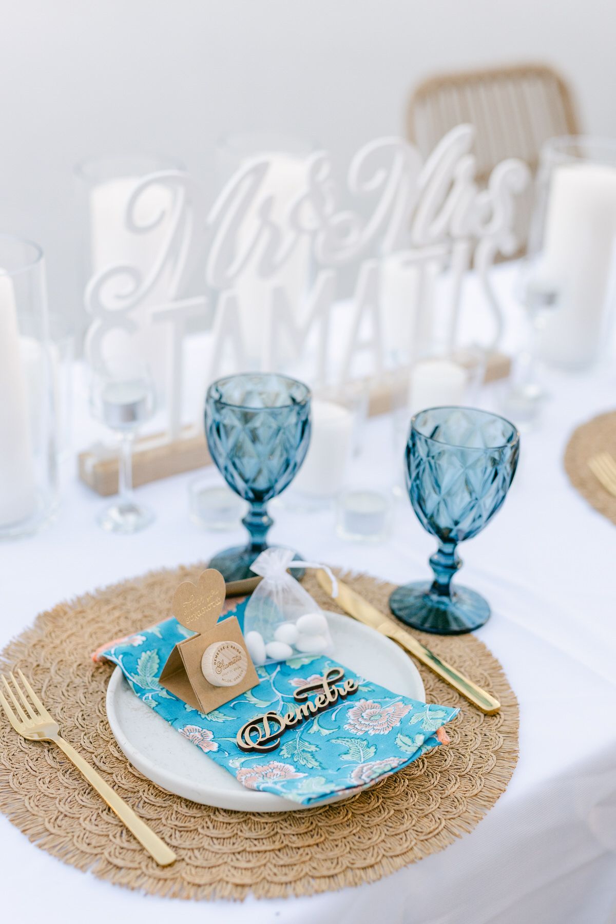 Elegant blue vintage wine glasses and place setting with gold accents on white tablecloth and woven charger plate.