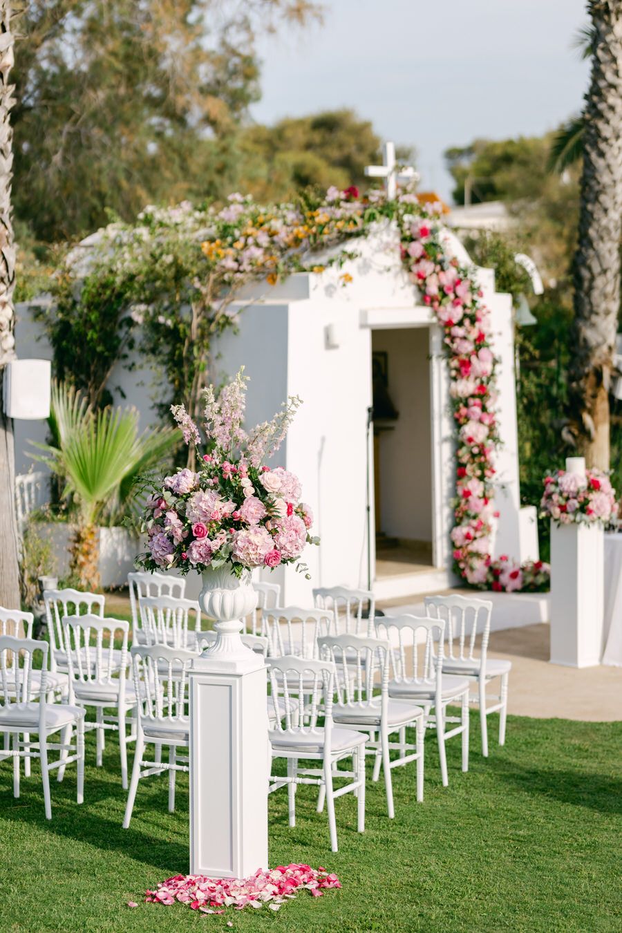 Elegant outdoor wedding ceremony setup with white chairs and floral arch decorated in pink roses.
