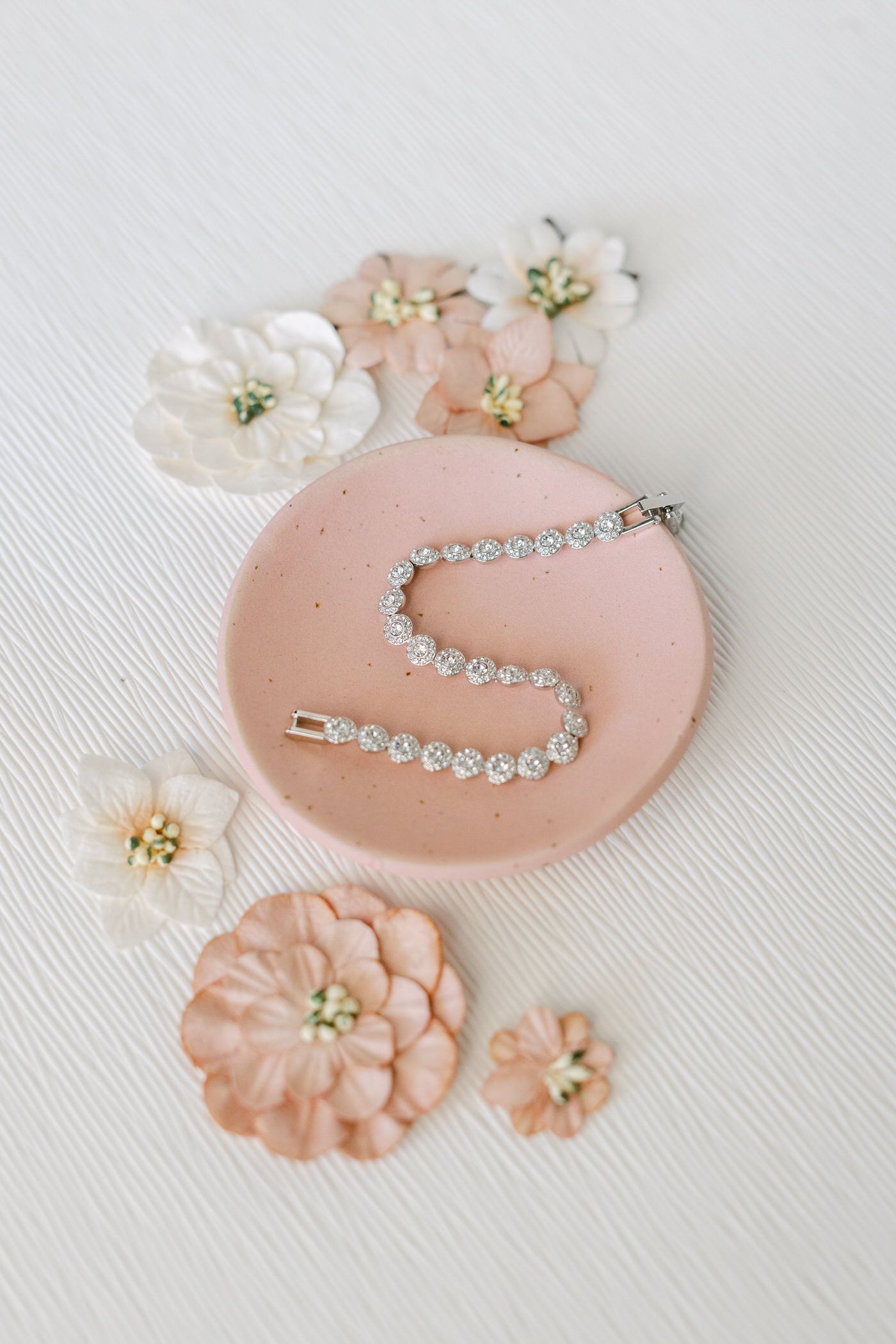 A delicate crystal bracelet displayed on a pink plate surrounded by soft peach and white floral decorations.