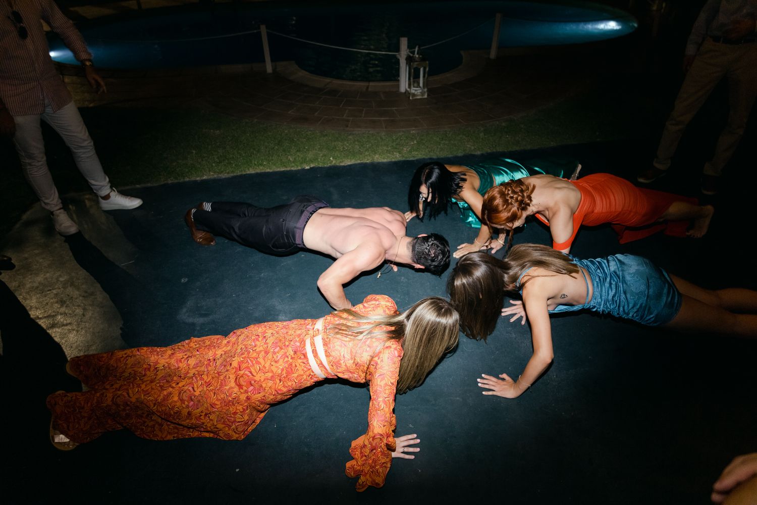 People lying on a dark blue mat during a night event or gathering, captured in dramatic lighting.