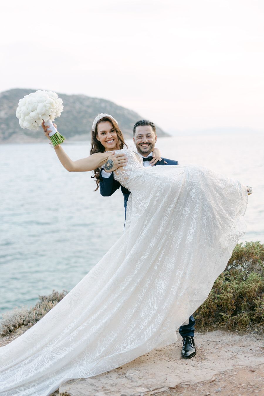 Romantic coastal wedding portrait with flowing white dress against ocean backdrop.