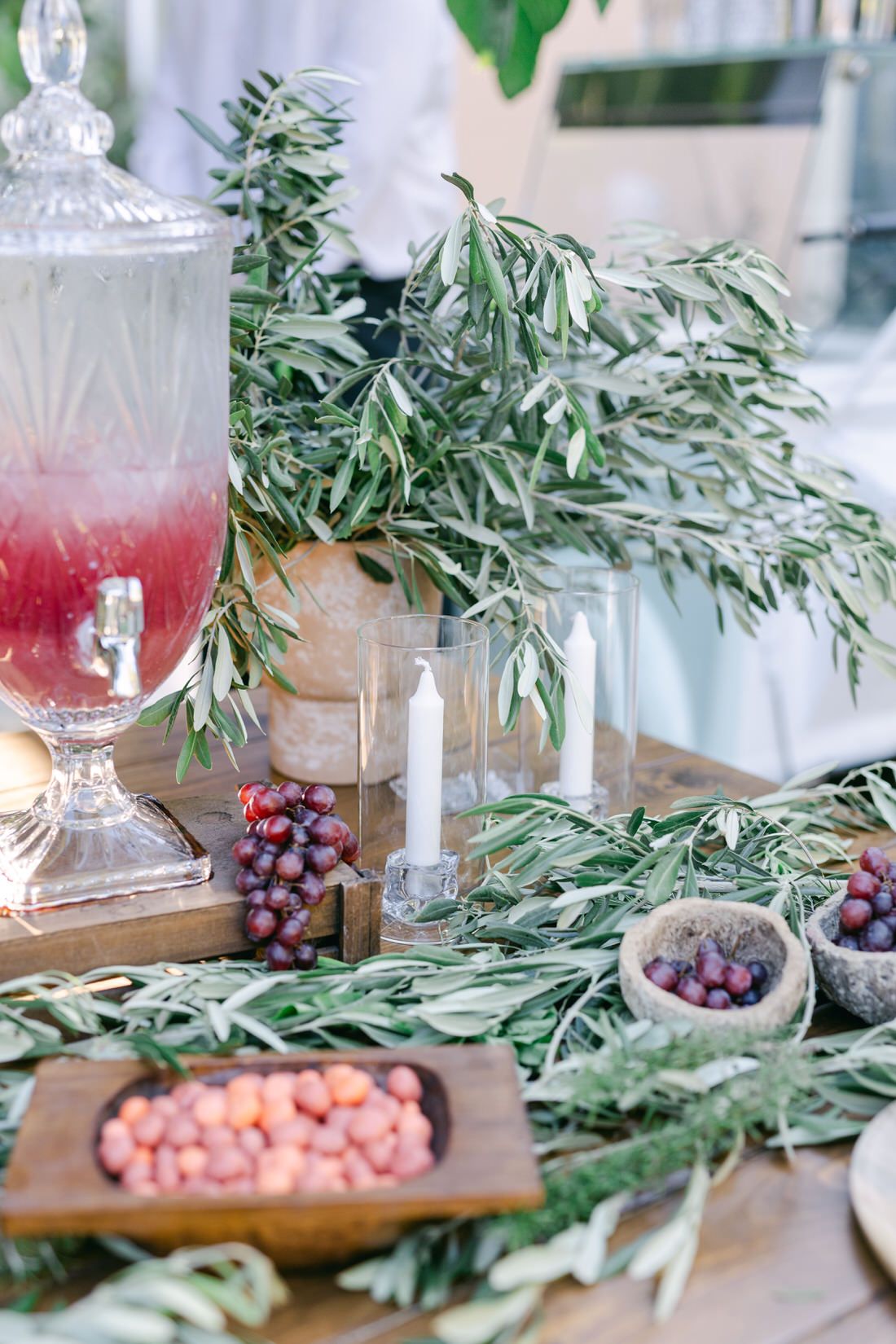 Elegant table setting with olive branches, pink candies, fresh grapes and crystal glassware with pink beverages.