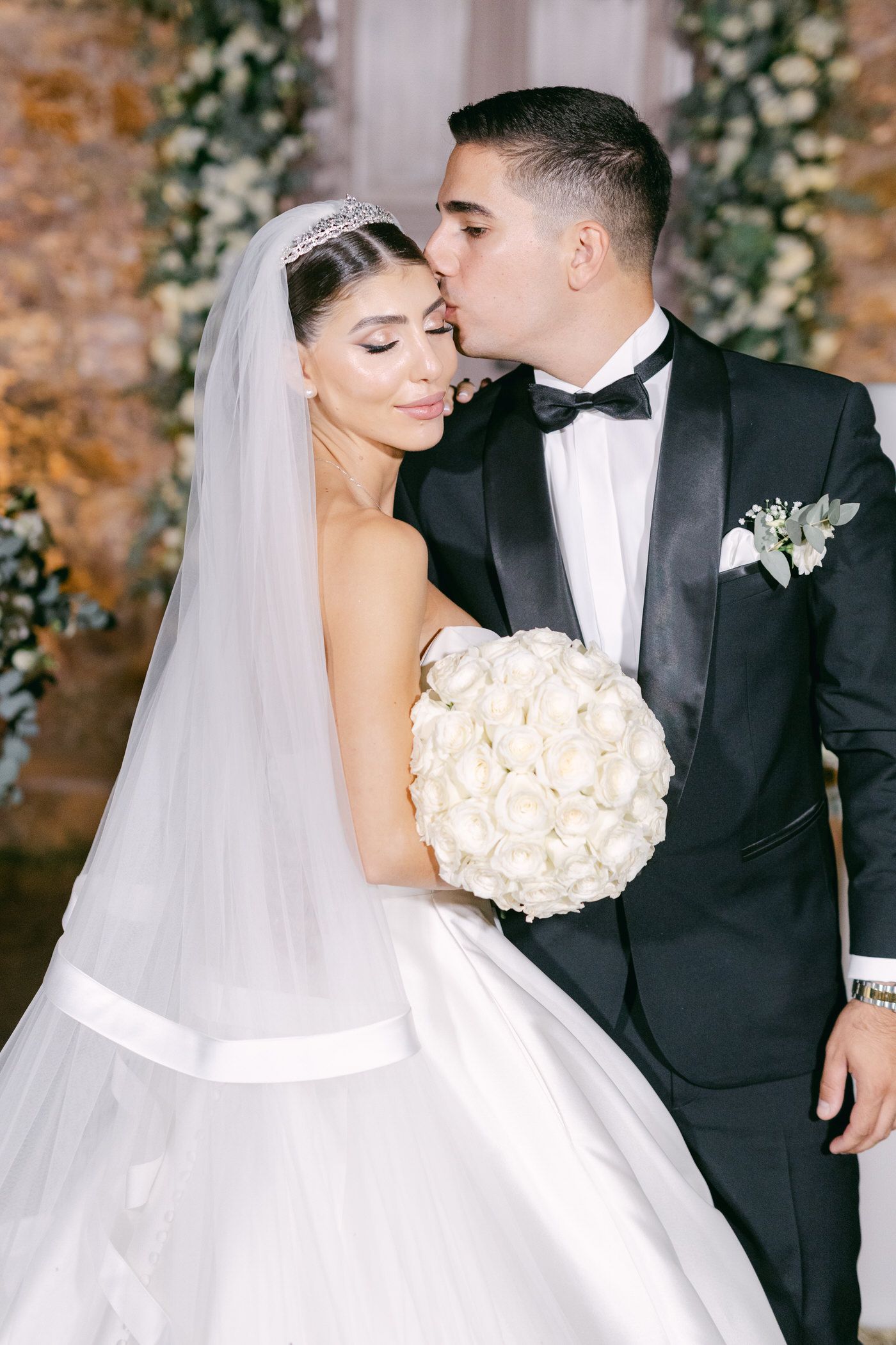 Classic black and white wedding portrait of newlyweds with a romantic pose against a floral backdrop.