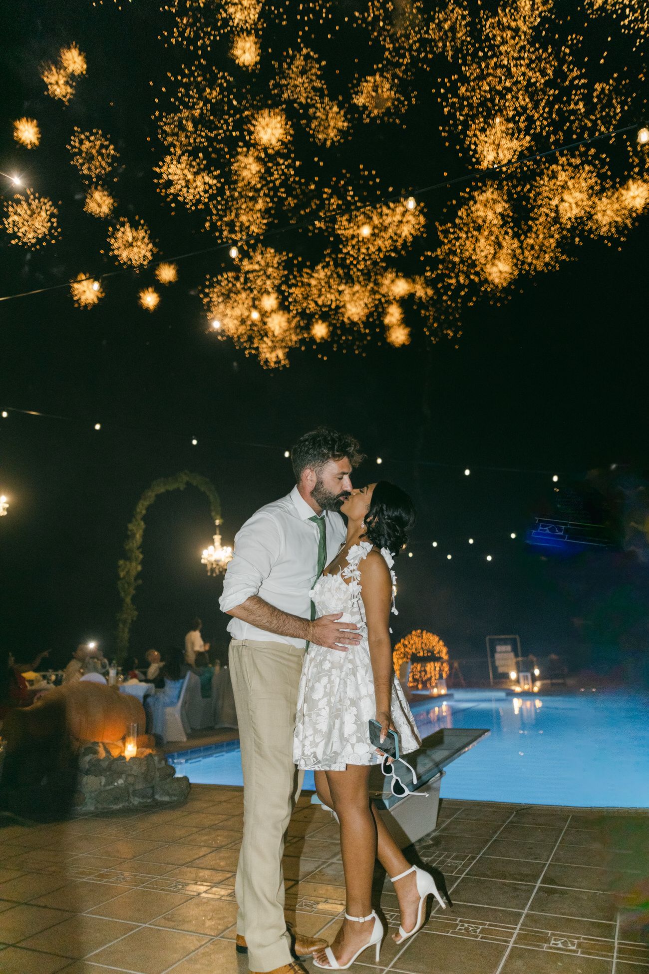 A romantic moment under golden lantern lights at a nighttime wedding reception.