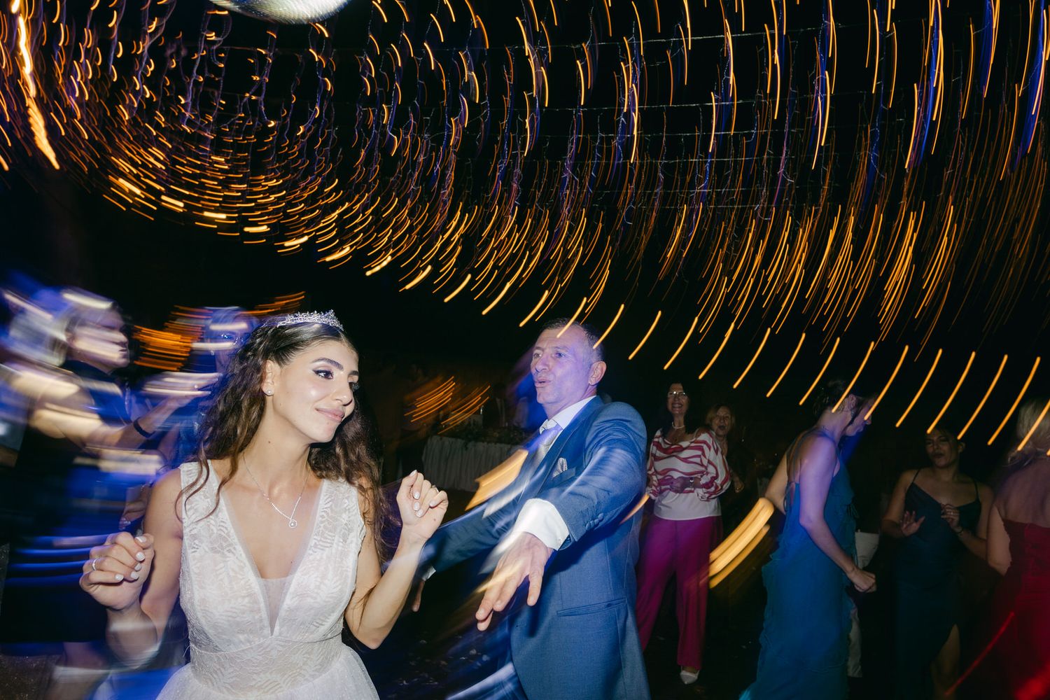People dancing and celebrating at an evening wedding reception with motion blur lights creating circular patterns overhead.