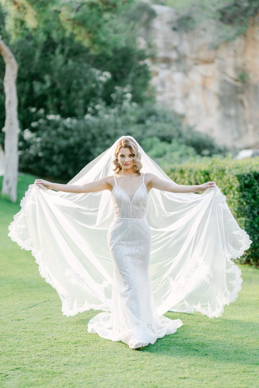 Bride displaying dramatic cathedral-length veil on manicured lawn.