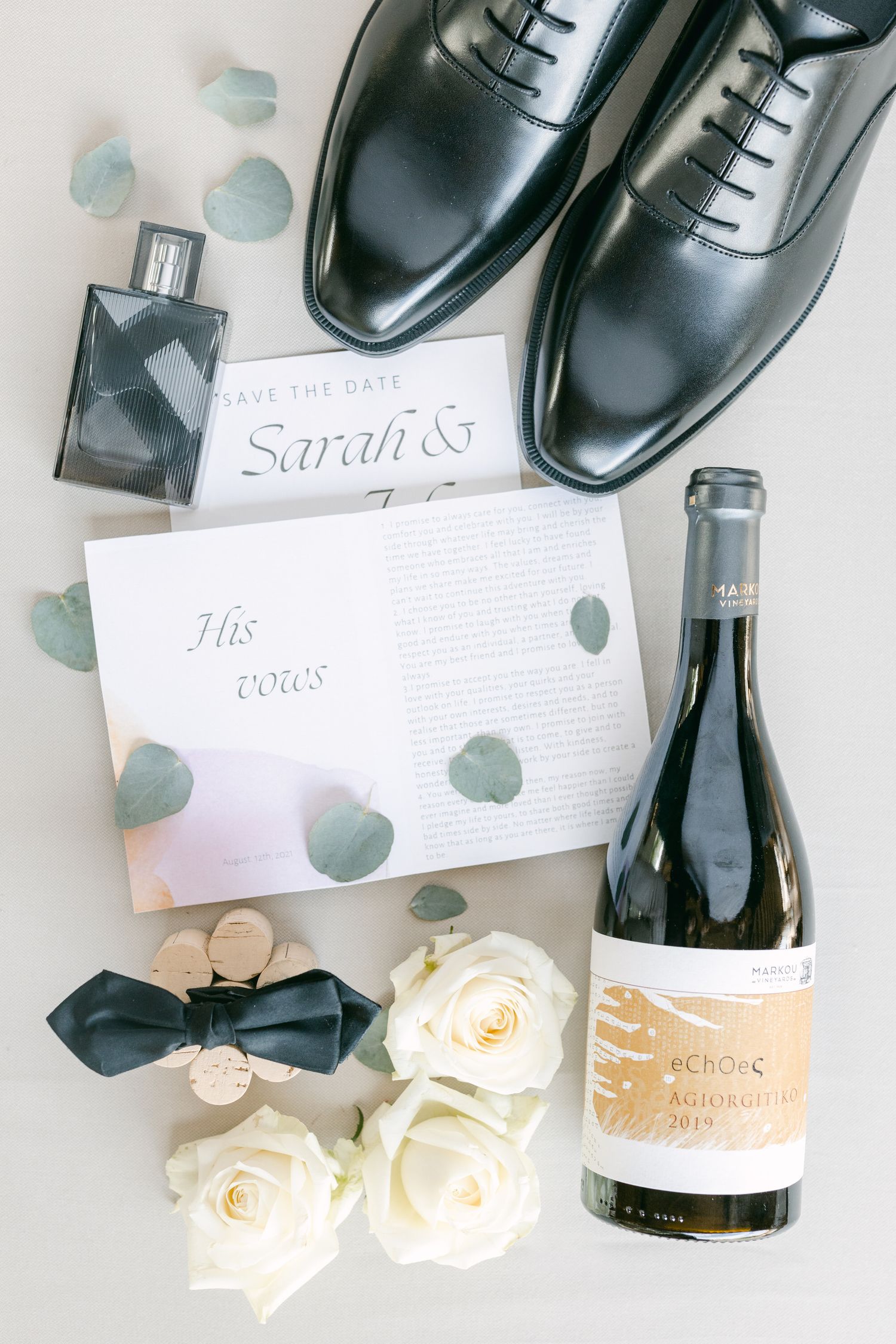 Wedding flat lay with black dress shoes, wine bottle, roses and invitation cards.