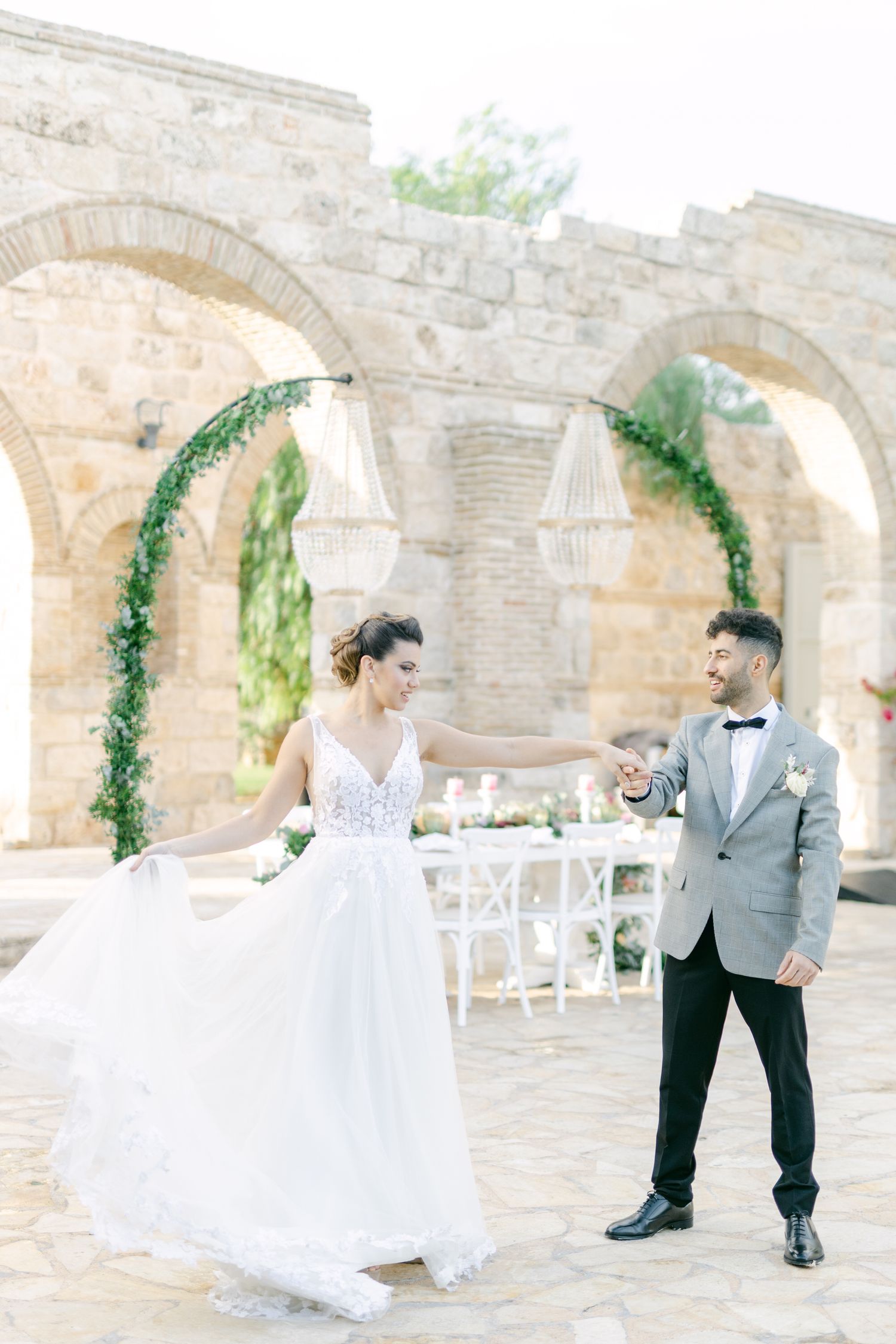 Wedding couple dances joyfully under stone arches decorated with hanging greenery.