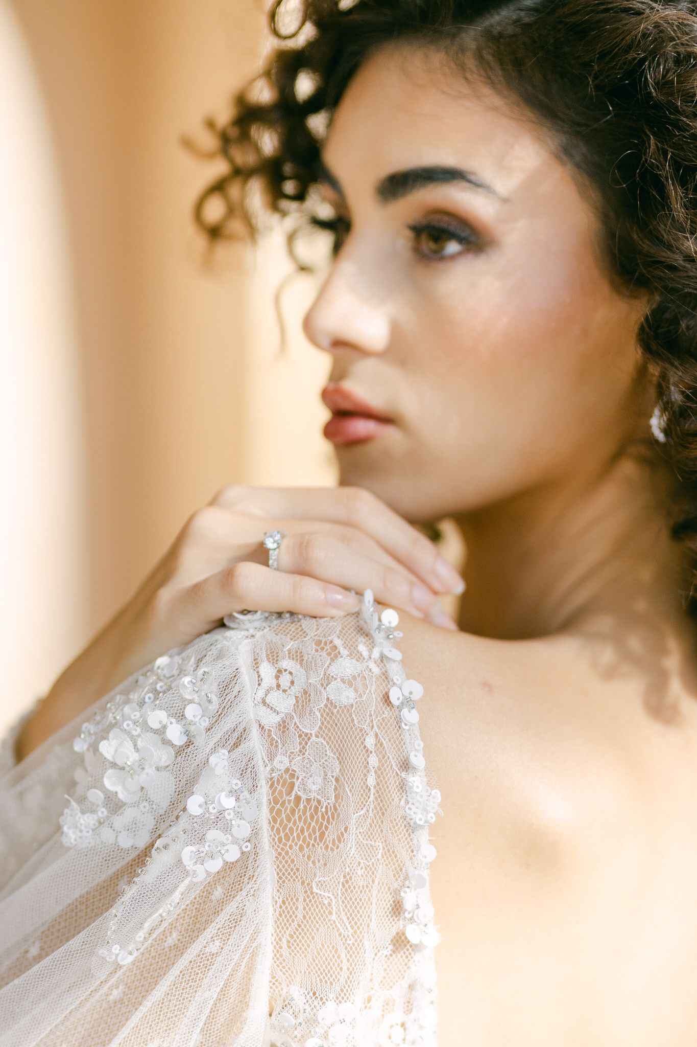 Ethereal bridal portrait showing delicate lace sleeve details and elegant ring in warm, dreamy lighting.