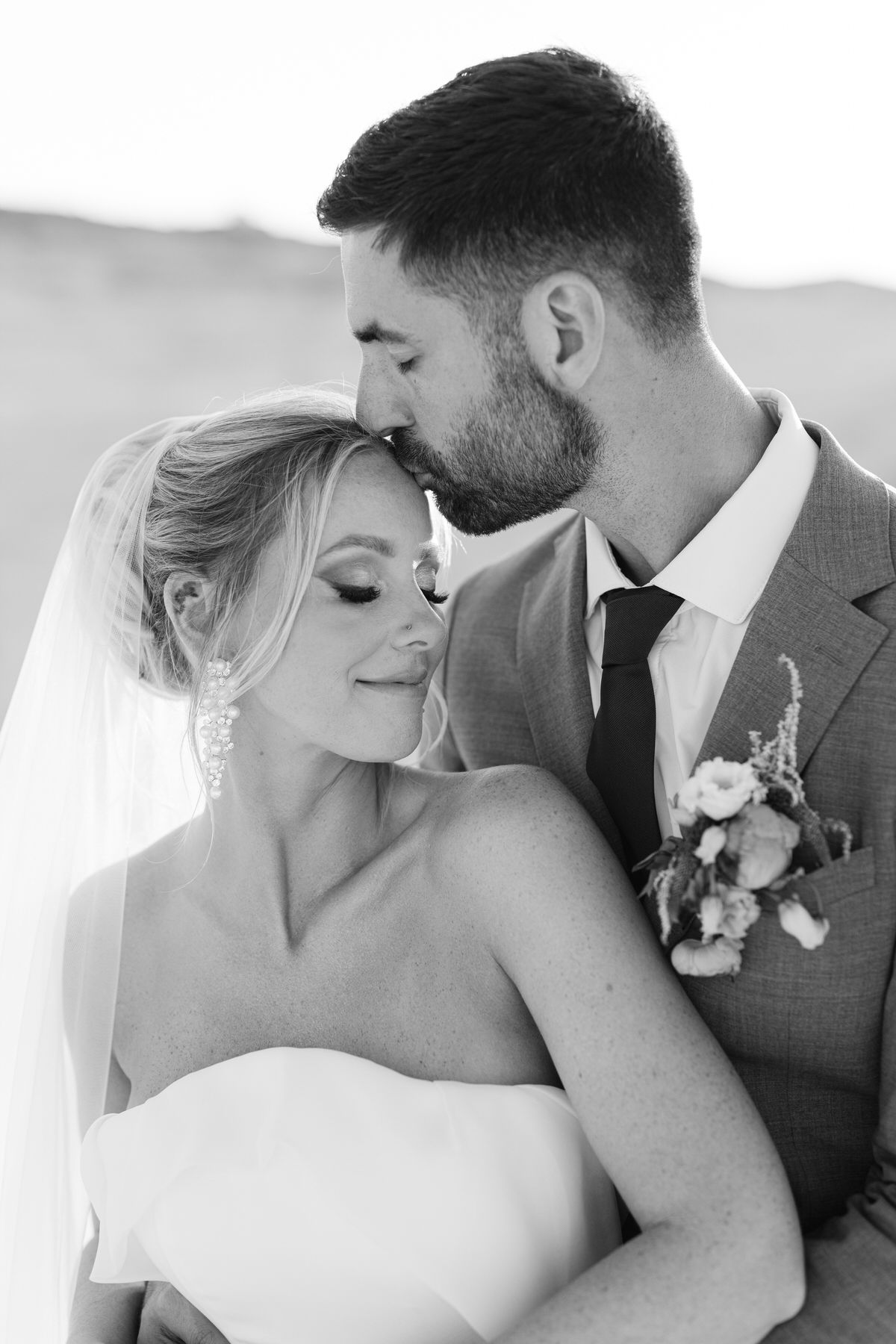 Romantic black and white wedding portrait of a tender moment between newlyweds with floral boutonniere detail.
