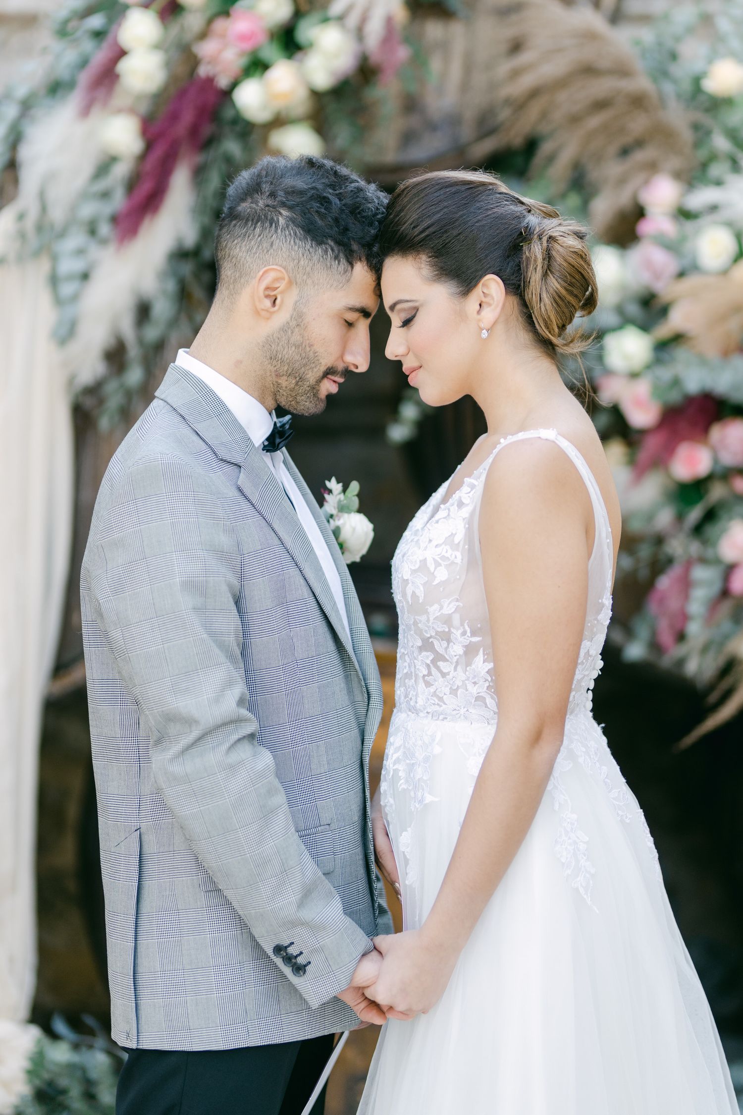 Romantic wedding couple sharing an intimate moment under a floral arch.