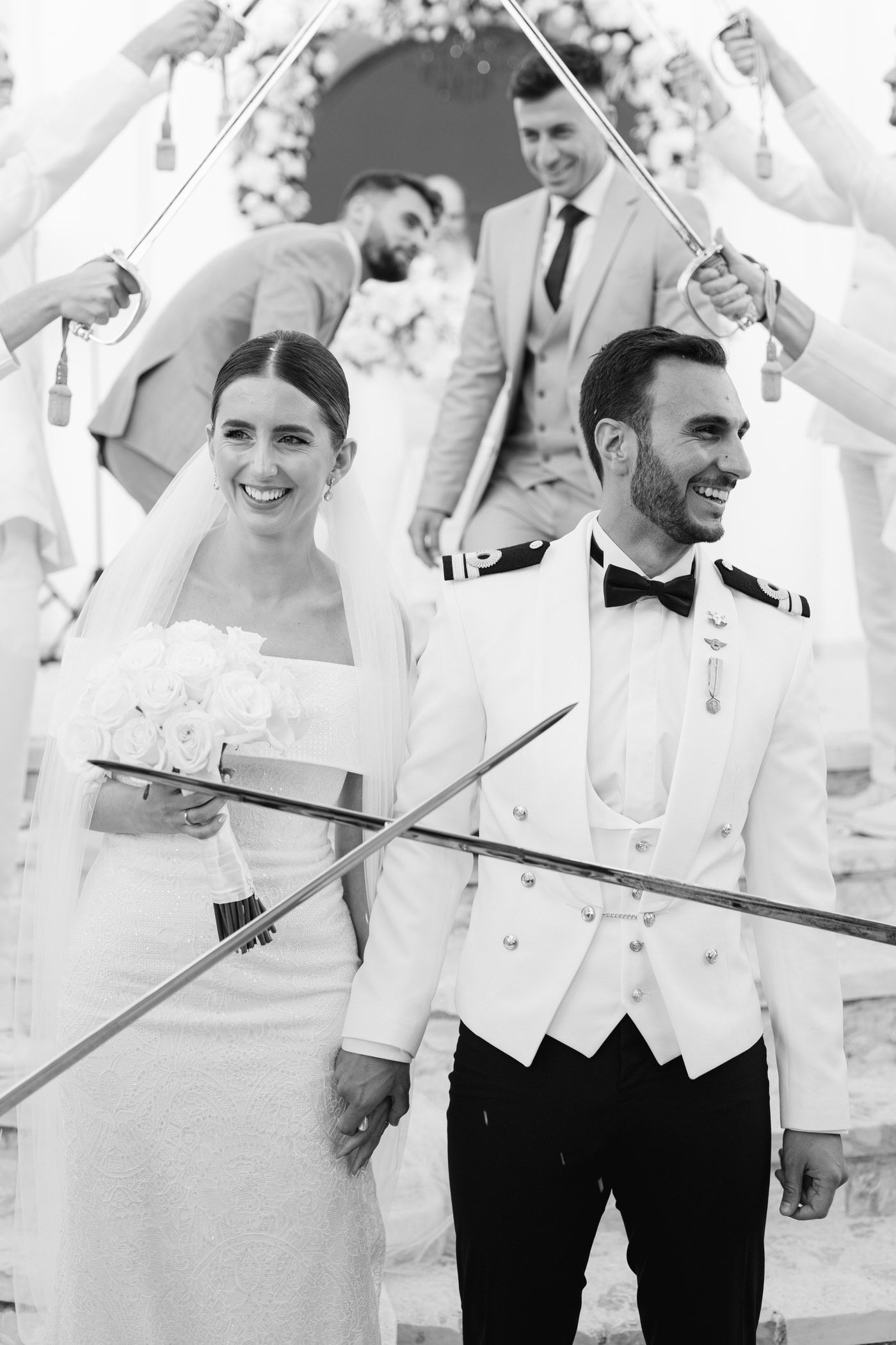 A joyful black and white wedding photo showing a couple walking under raised swords in a traditional military ceremony.