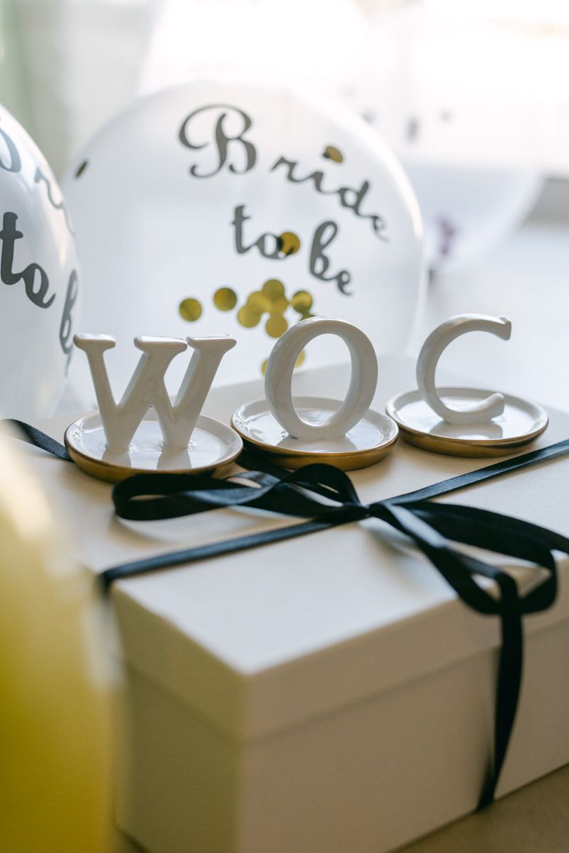 White decorative letters WOG and a balloon marked 'Bride to be' with a black ribbon tied gift box in soft lighting.