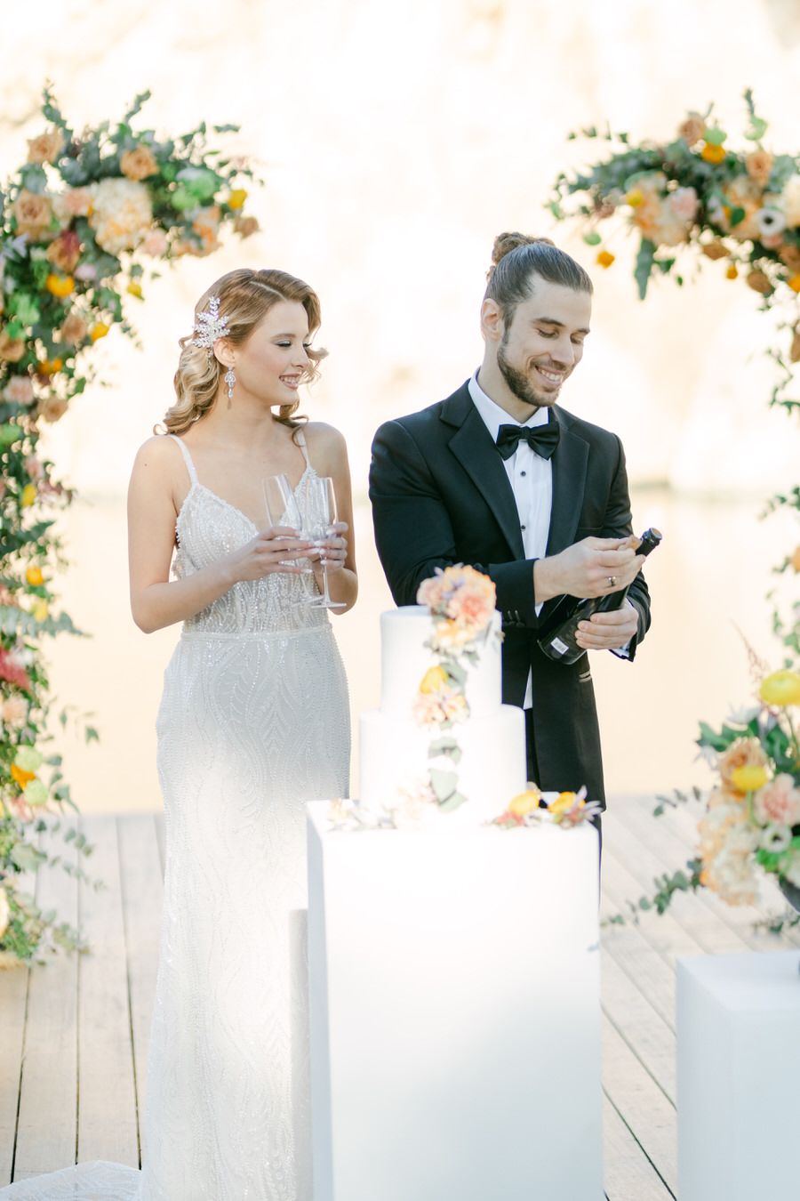 Elegant wedding couple in formal attire checking their phones during outdoor ceremony surrounded by floral decor.