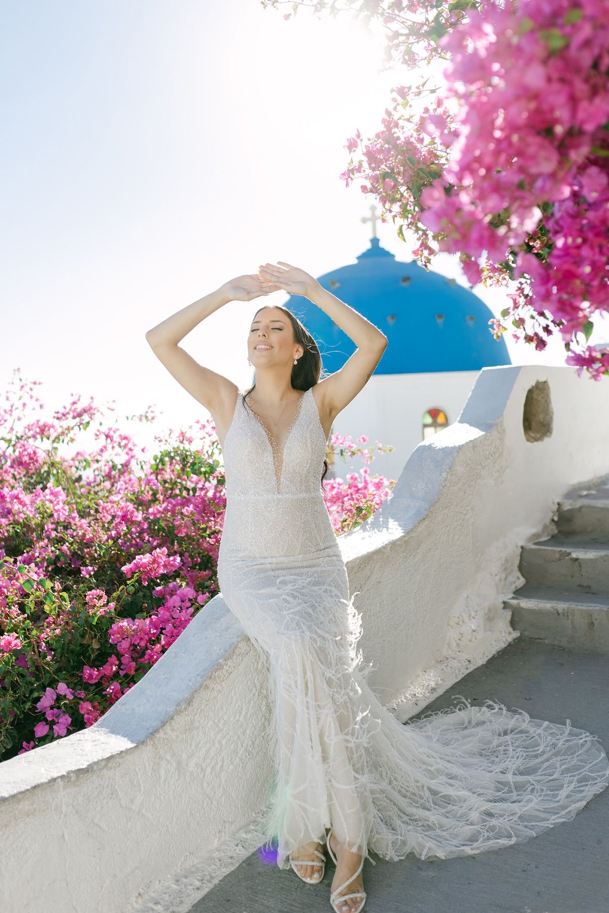 A bride in a flowing white lace dress twirls joyfully against a backdrop of vibrant pink bougainvillea flowers.