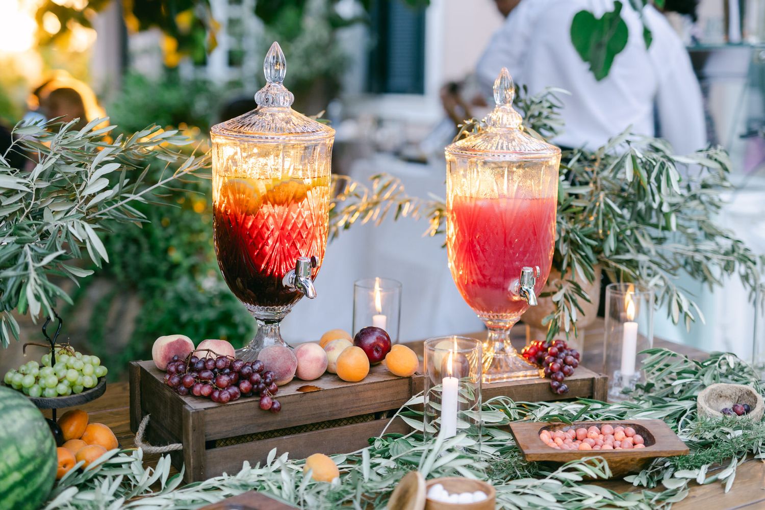 Elegant cocktails and appetizers displayed on a table with greenery and decorative ornate glassware at sunset.