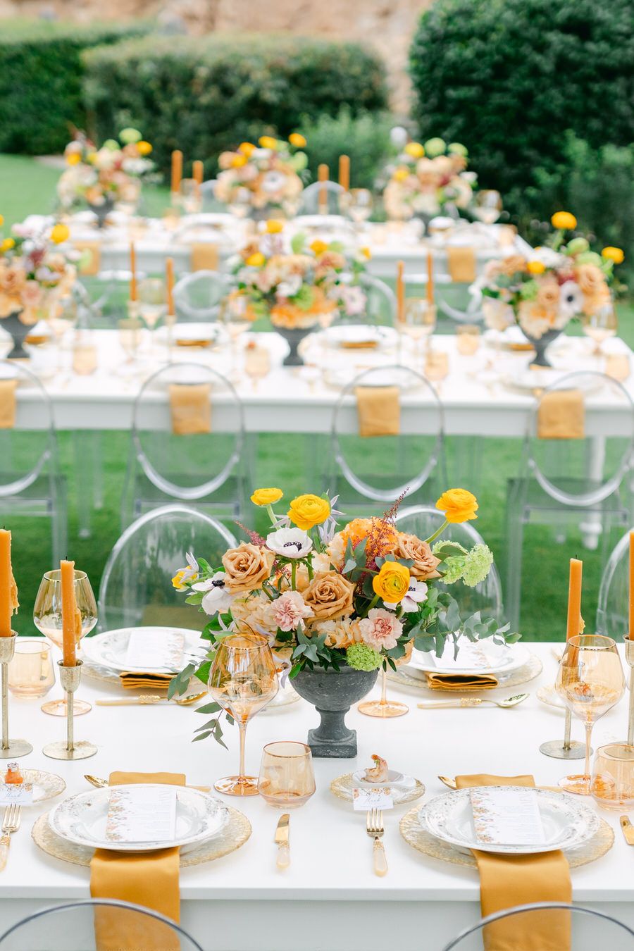 Wedding reception tables with orange and yellow floral centerpieces and gold accents.