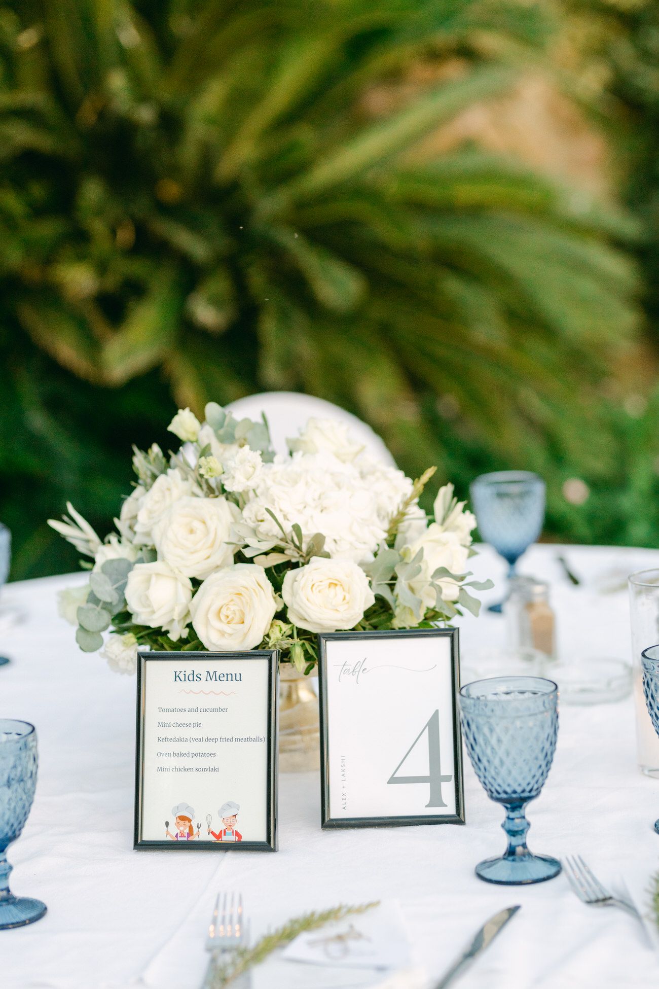 An elegant wedding table setting with white roses and blue glassware.
