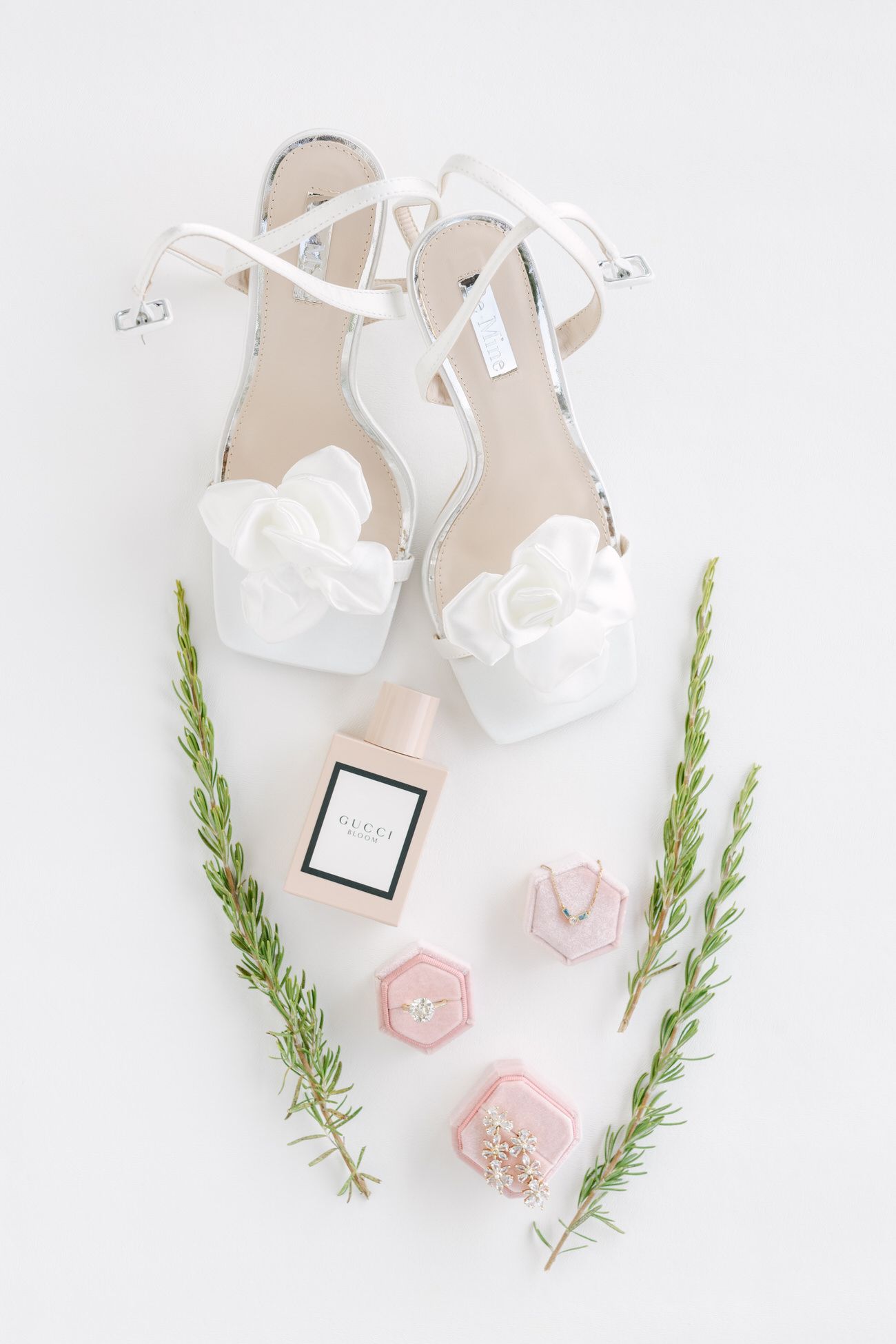 White bridal sandals with floral details styled with pink boxes and greenery on white background.