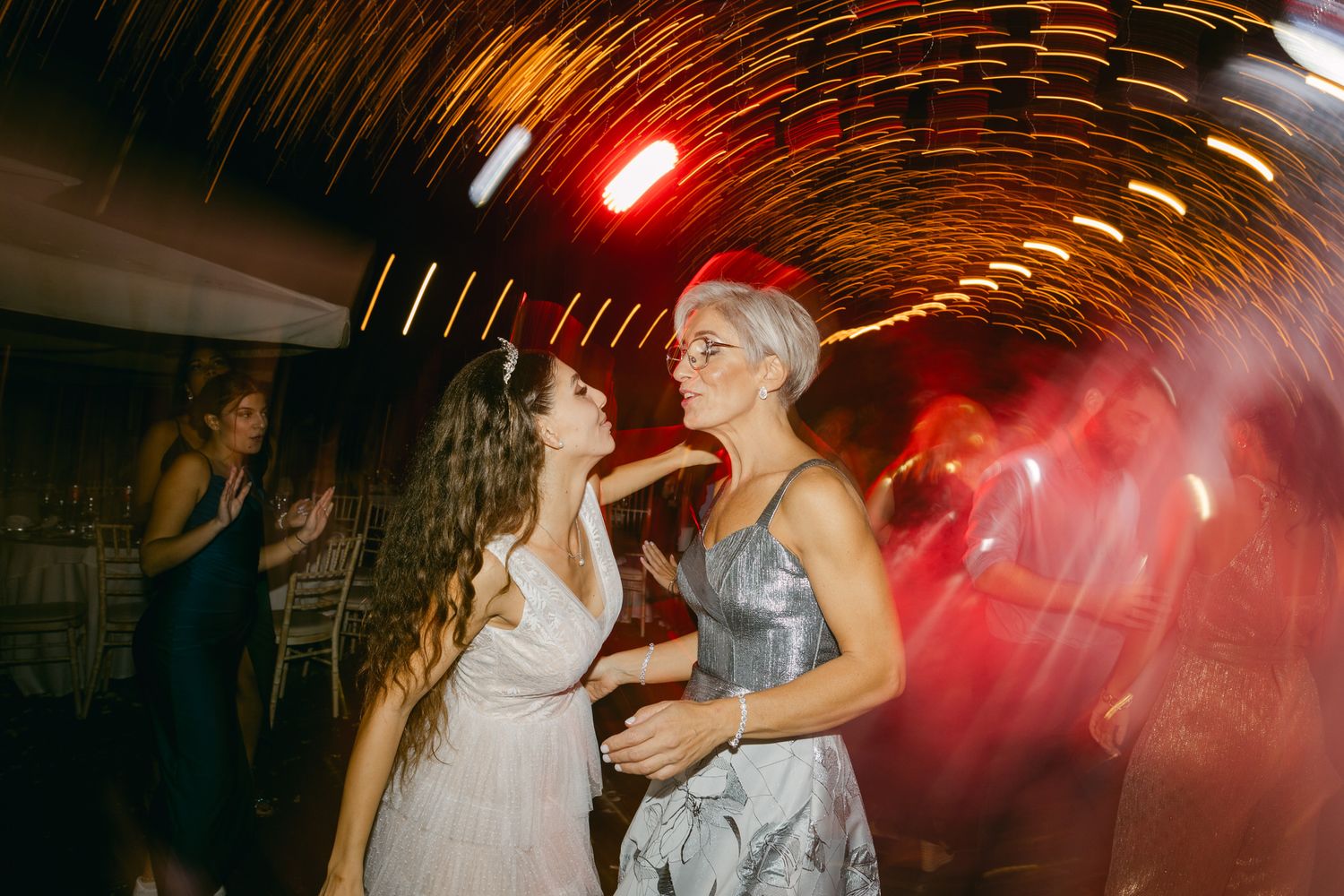 Guests dancing at a nighttime celebration with motion blur and red lighting effects in the background.