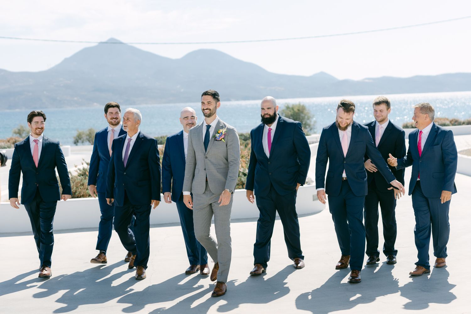 Group in formal attire walking together against mountain backdrop on sunny day.
