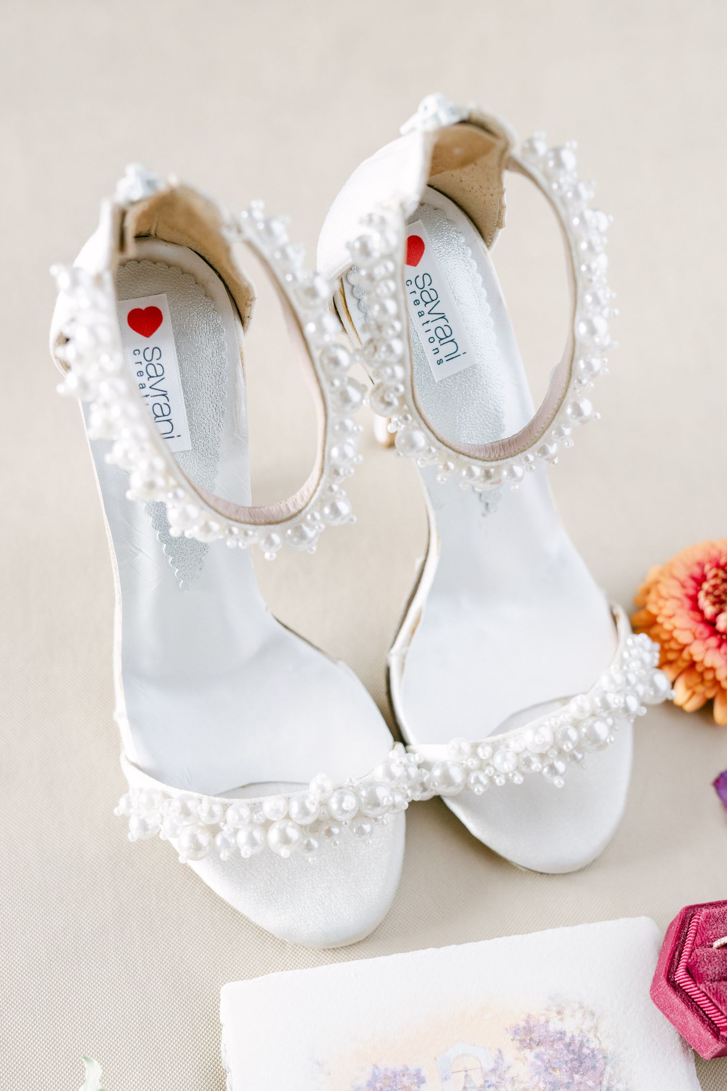Elegant white bridal sandals adorned with delicate pearl details along the straps on a light beige background.