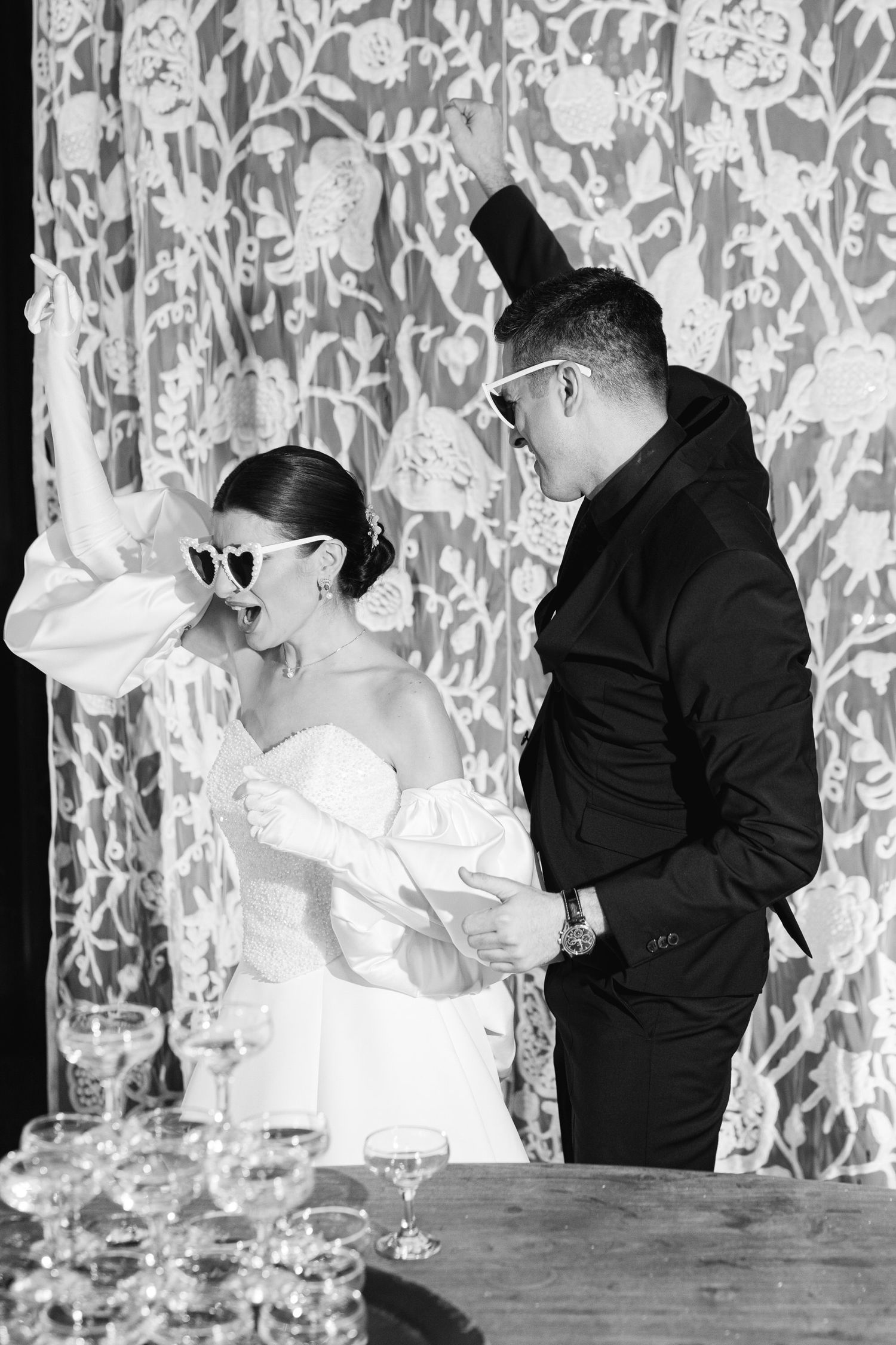 Black and white photo of a couple in formal wear sharing a moment against a patterned backdrop at a celebration.