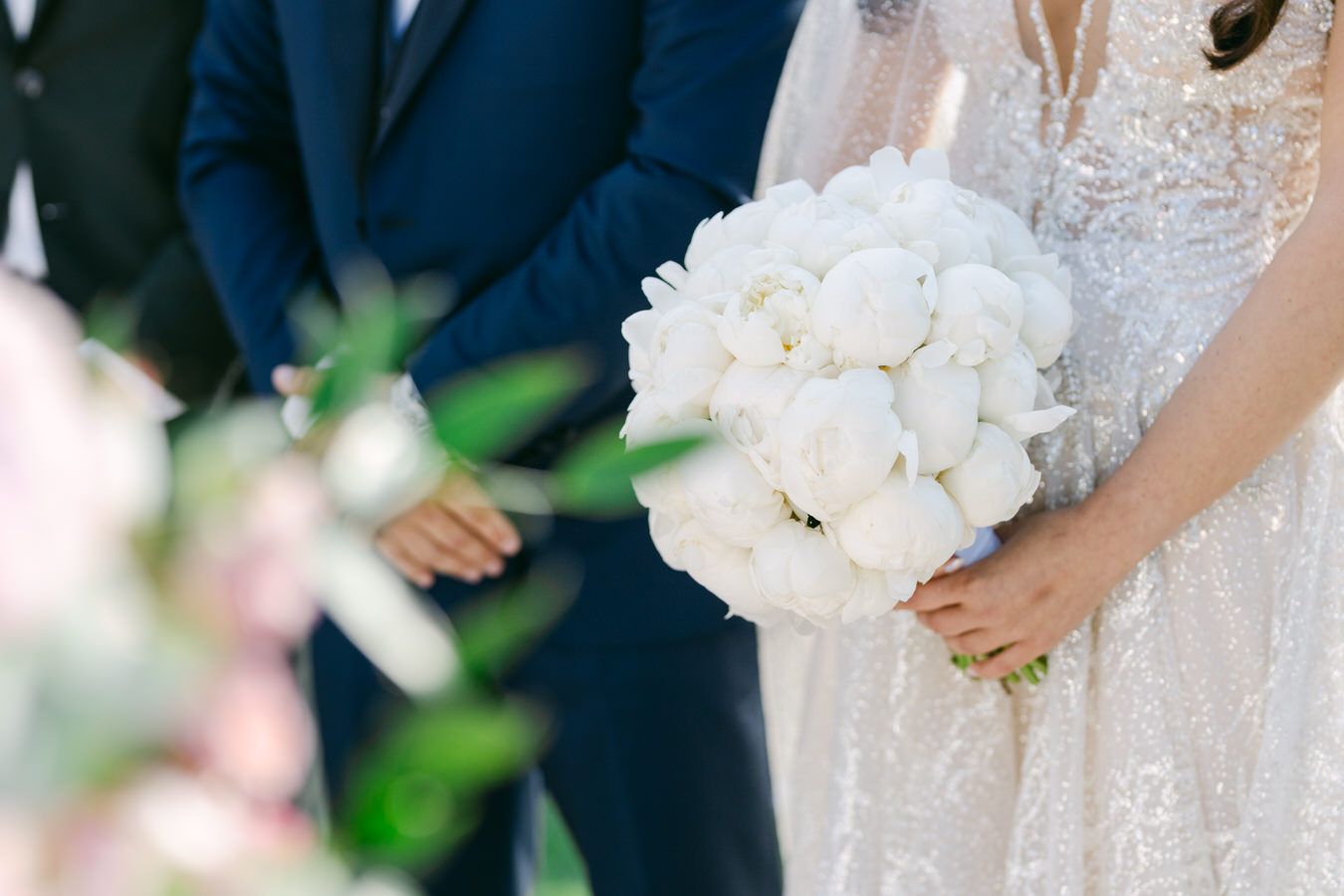 Close-up of elegant white rose bridal bouquet against lace wedding dress.