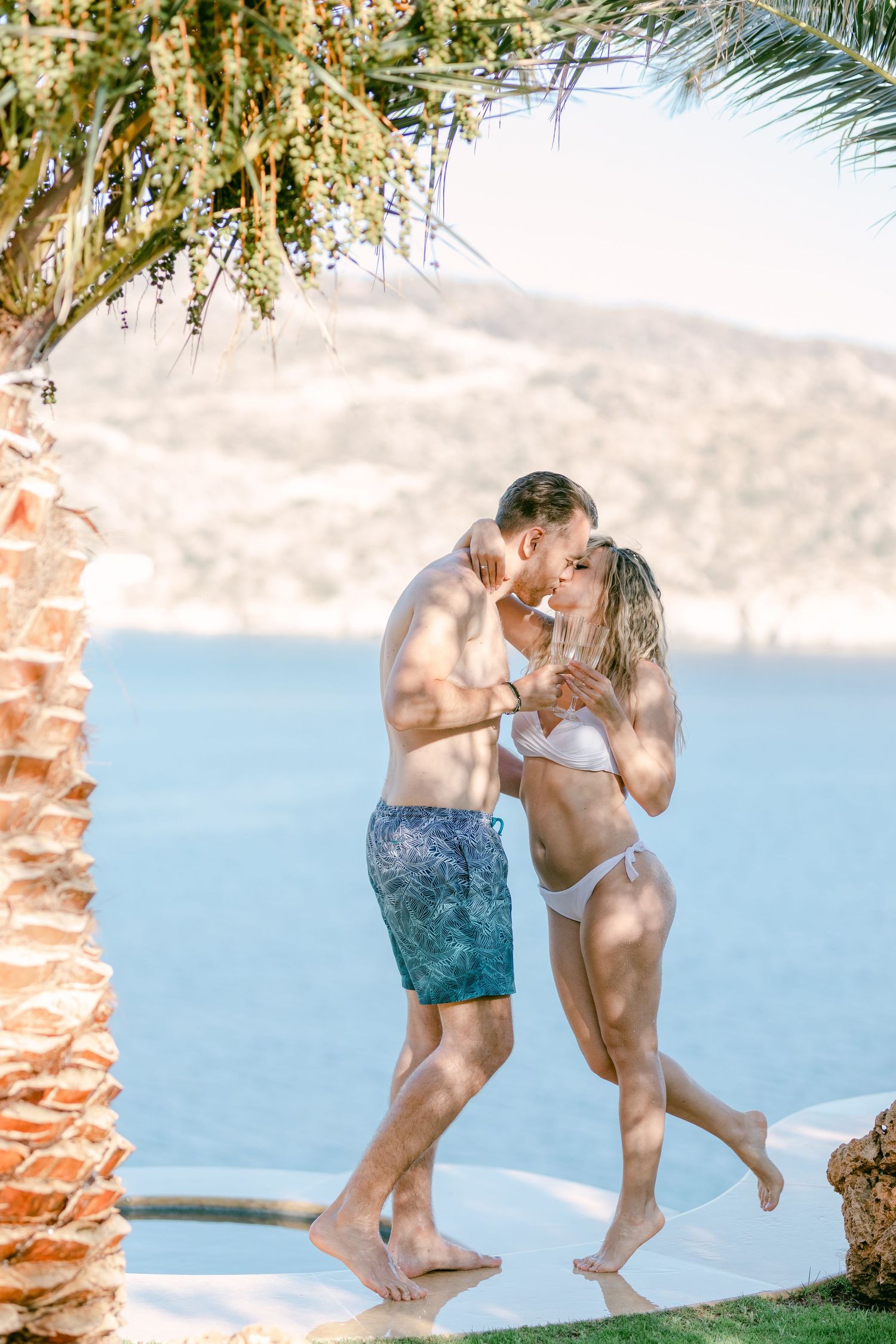 Couple sharing intimate moment by palm tree with ocean view background.