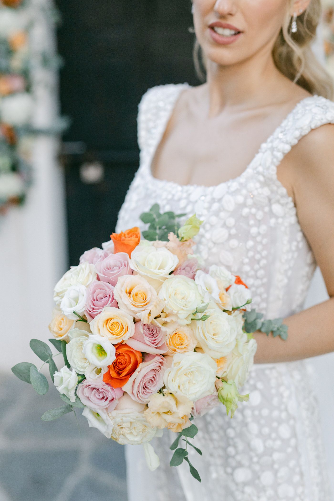 Close up of a bridal bouquet with peach, white and pink roses with eucalyptus leaves against a lace wedding dress.