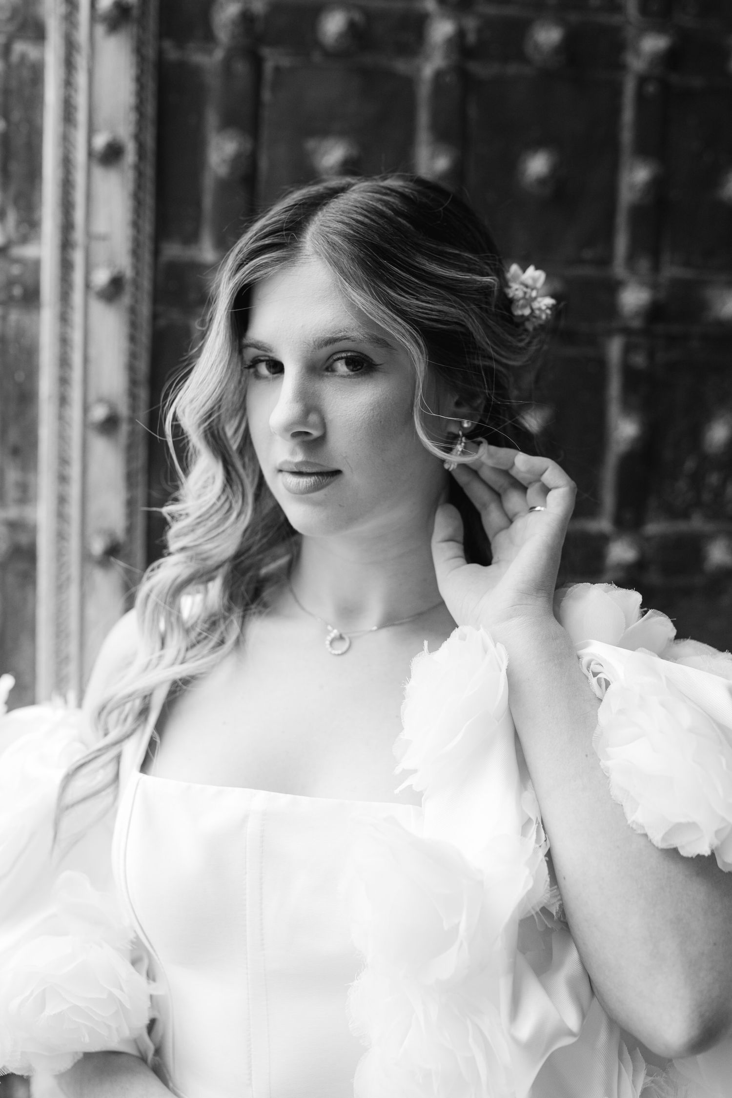 Black and white portrait of a young subject in a romantic white dress with puffy sleeves and small floral hair accessories.