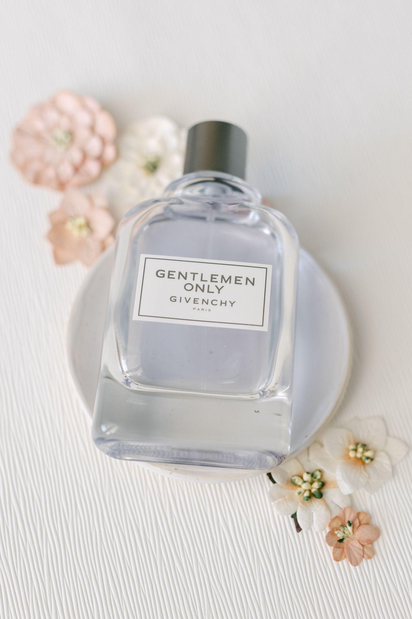 Gentlemen Only fragrance bottle on white surface with delicate pink and white floral decorations.
