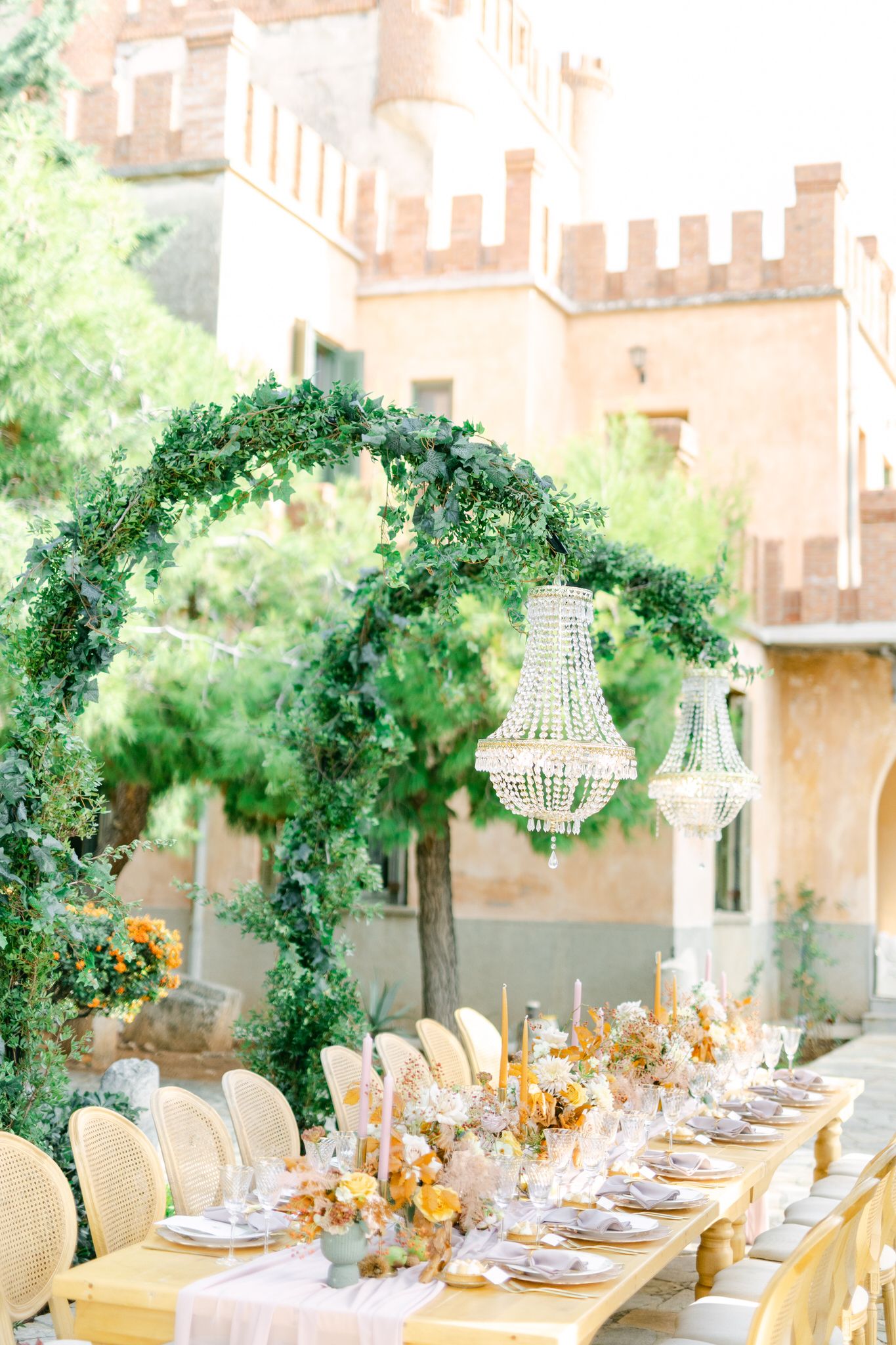 Elegant outdoor wedding table setting with crystal chandelier and greenery arch at a Mediterranean villa estate.