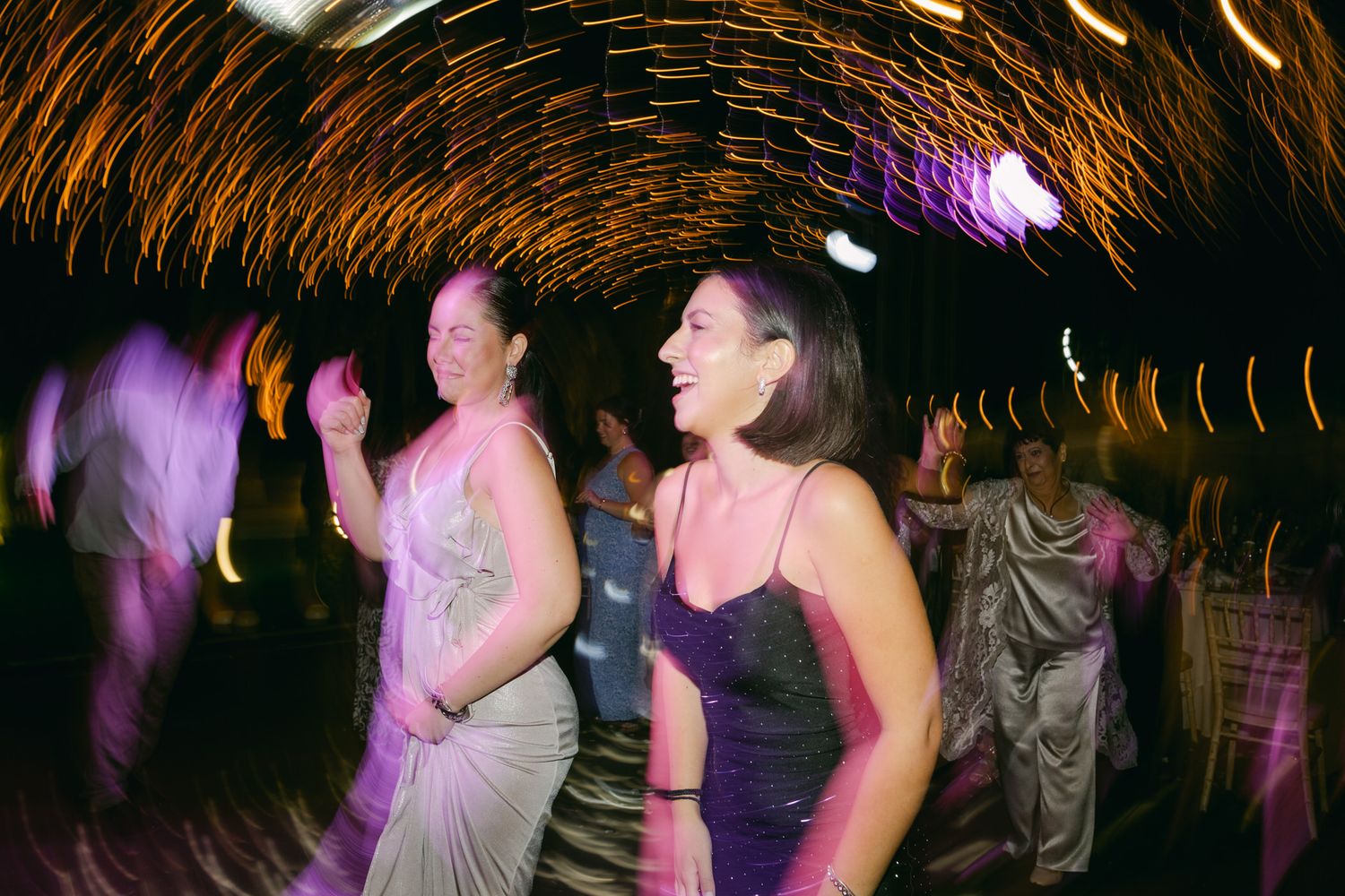 People dancing at a nightclub with swirling light trails and purple lighting effects creating a dynamic party atmosphere.