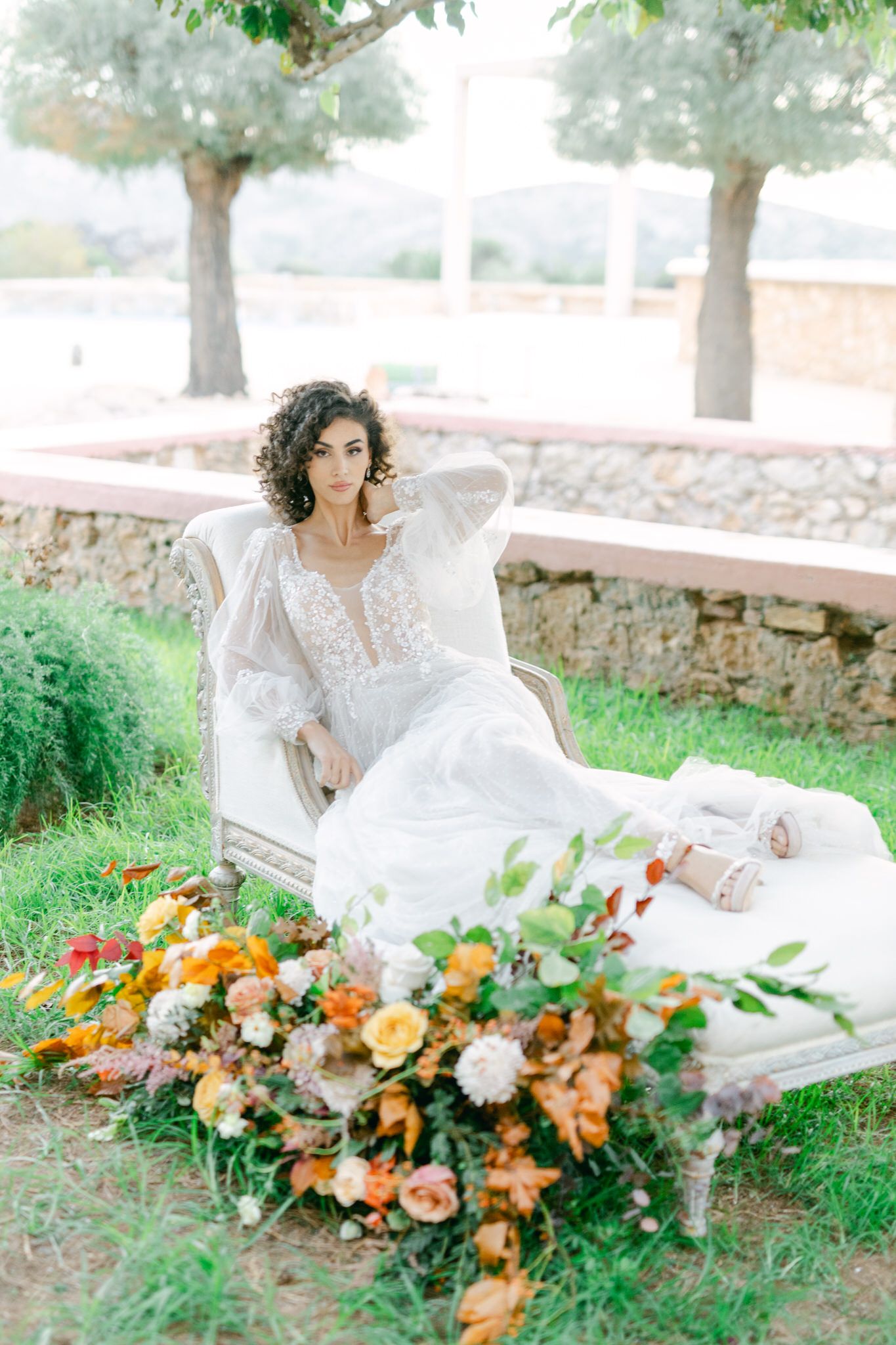 Ethereal bridal portrait in a garden setting with a romantic white dress and vibrant orange and peach floral arrangement.