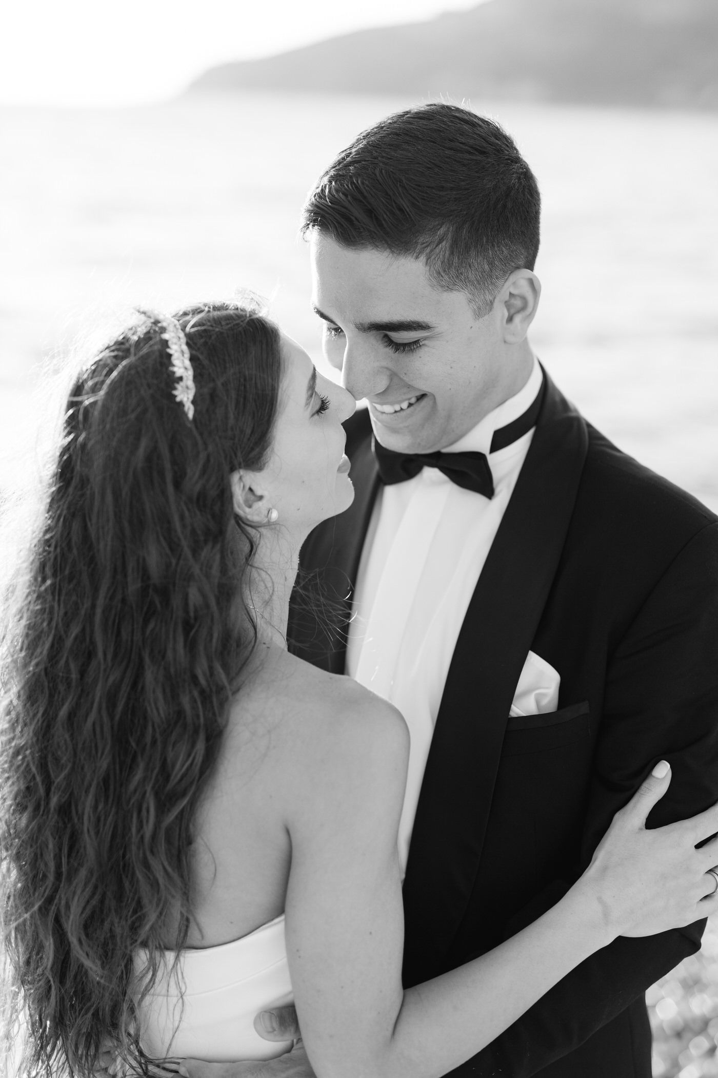 A romantic black and white portrait of a bride and groom sharing an intimate moment in formal wedding attire.