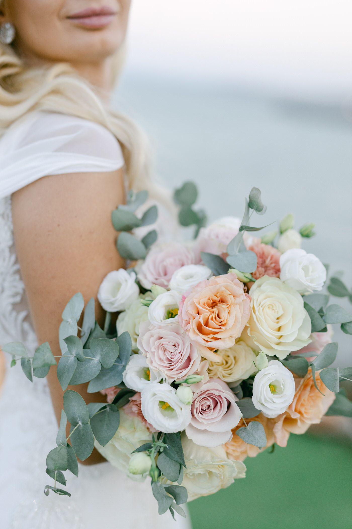 A romantic bridal bouquet featuring peach, blush pink and white roses with silver-green eucalyptus leaves.
