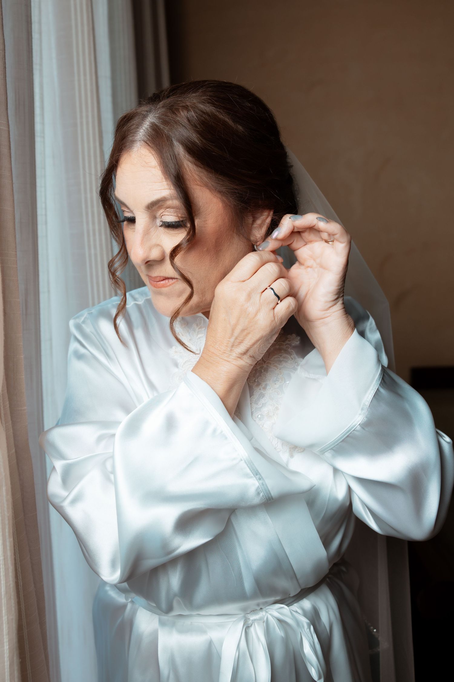 Person in white satin robe getting ready in a series of candid photos by a window.