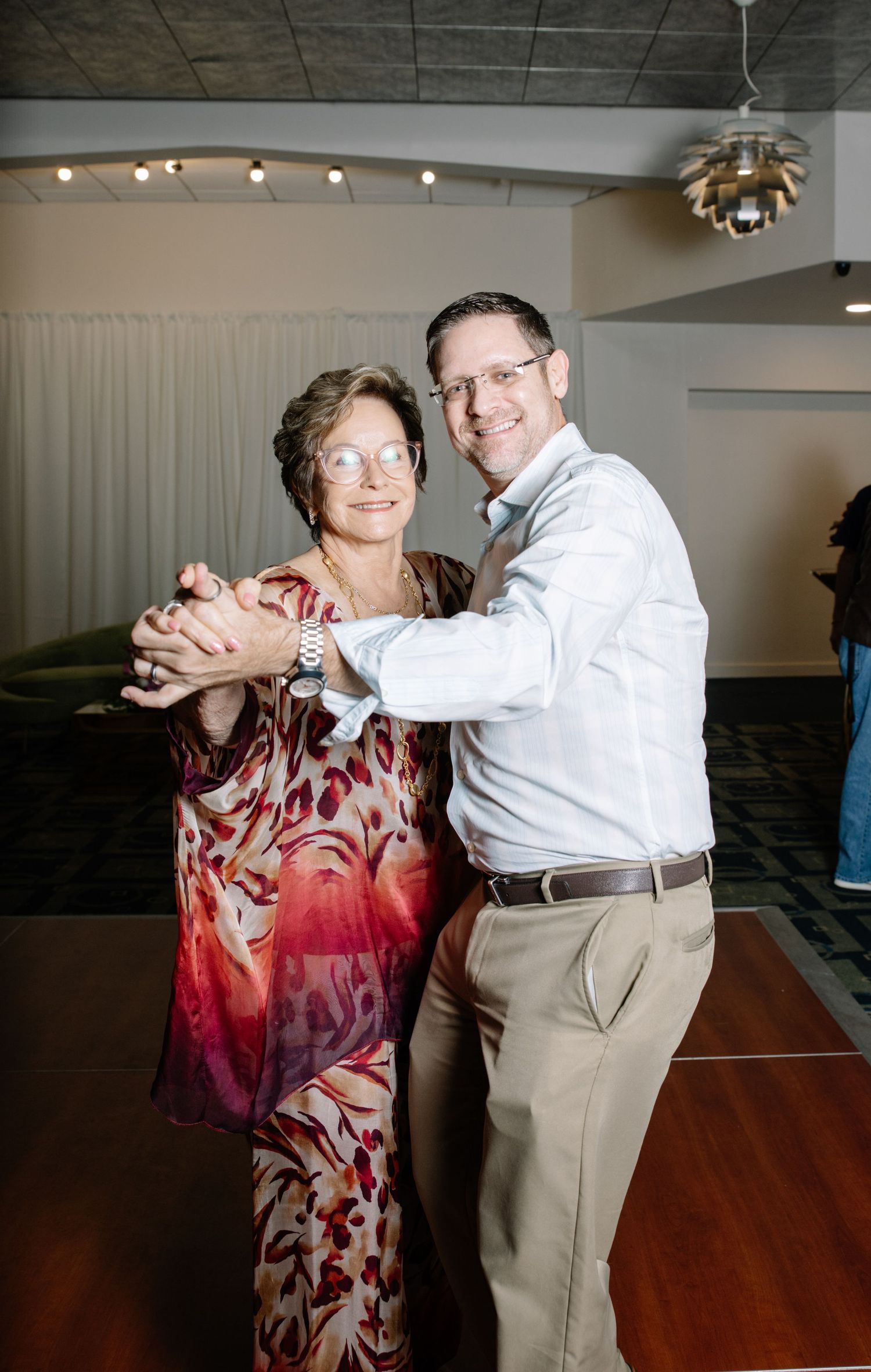 Couple dancing together on wooden floor at social gathering.
