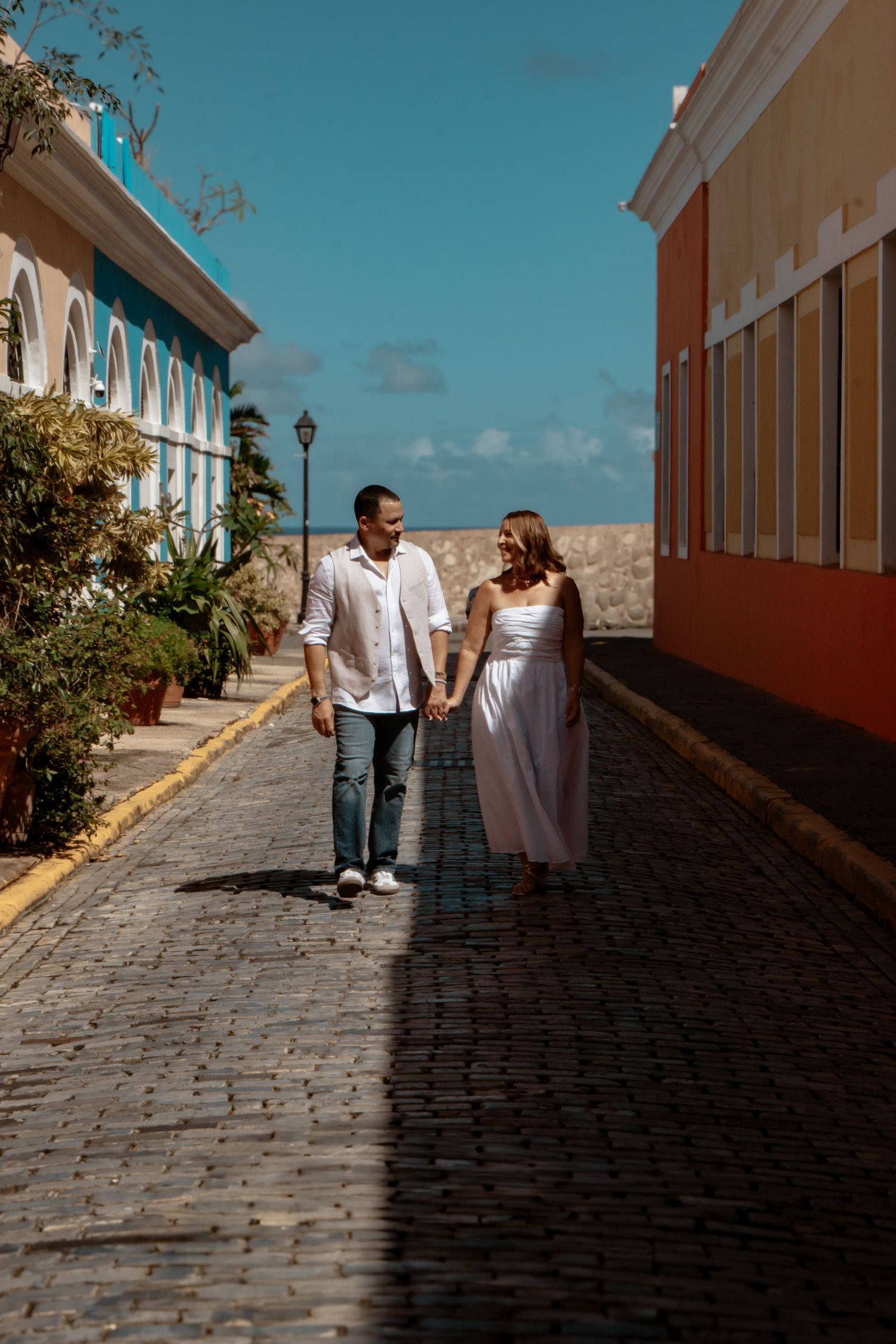 Couple walking down a cobblestone street with colorful colonial buildings.