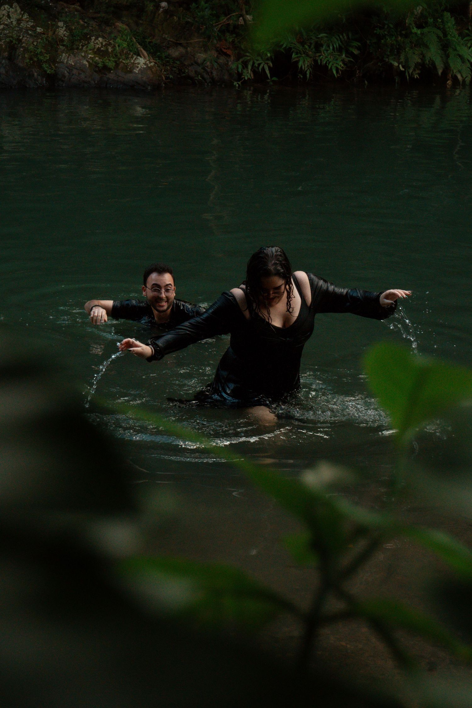 A couple splashes playfully in dark green water during a photo session.