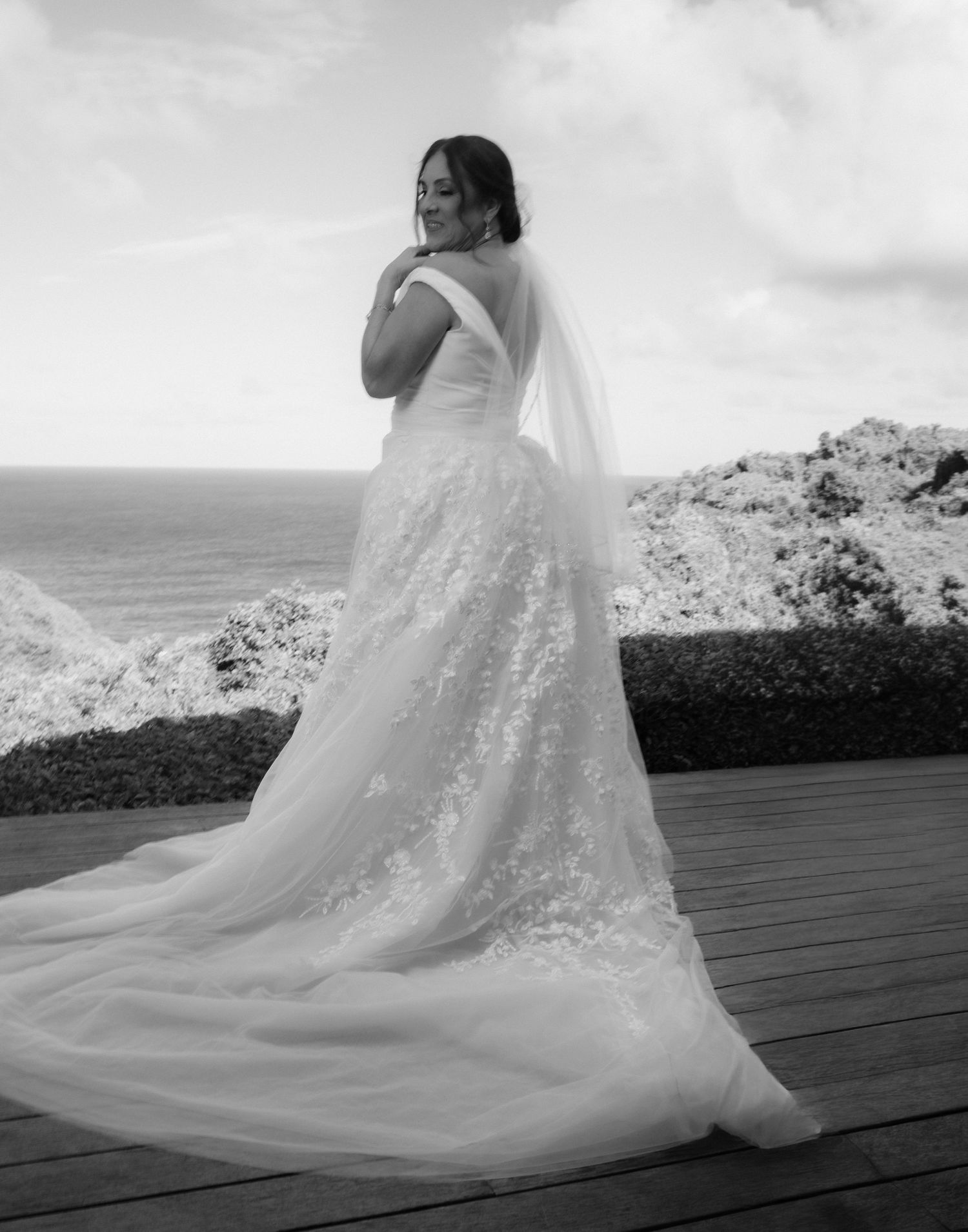 A sequence of black and white photos showing a flowing wedding dress train on a wooden deck overlooking the ocean.