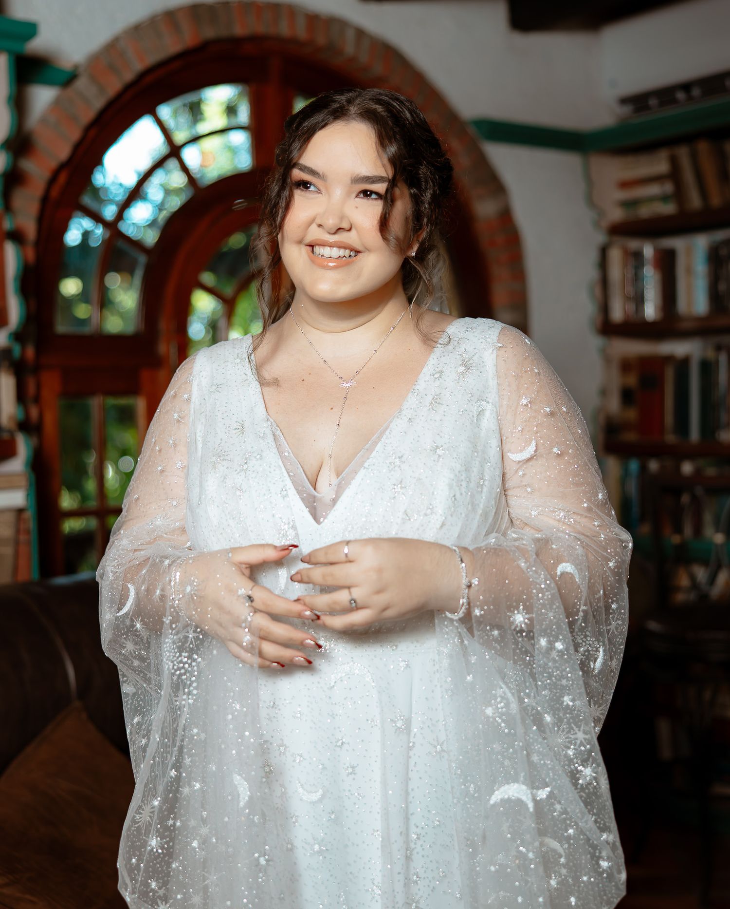 Smiling bride in white celestial moon and star embroidered wedding gown poses indoors.