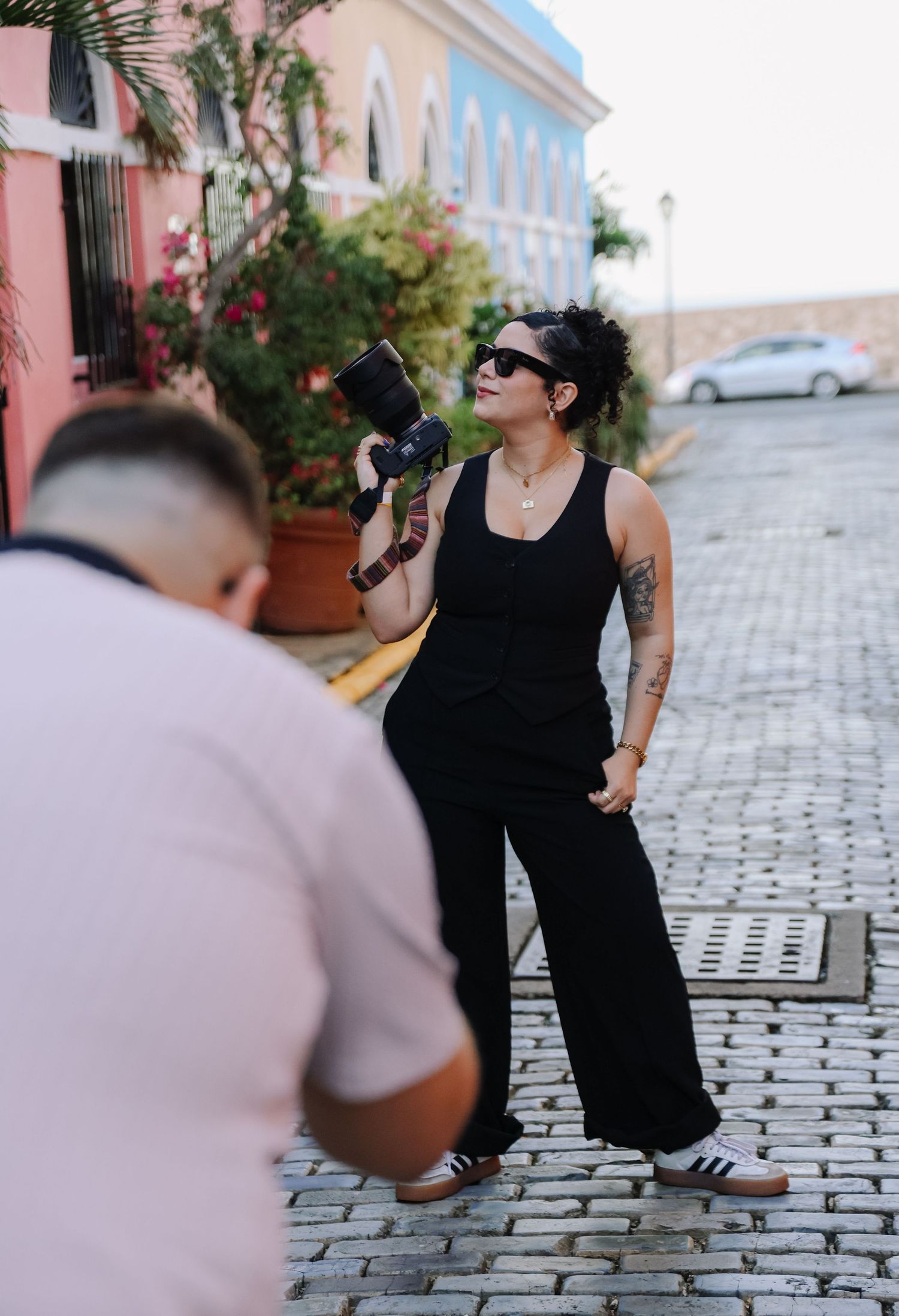 Photographer in black attire working on cobblestone street with colorful colonial buildings.