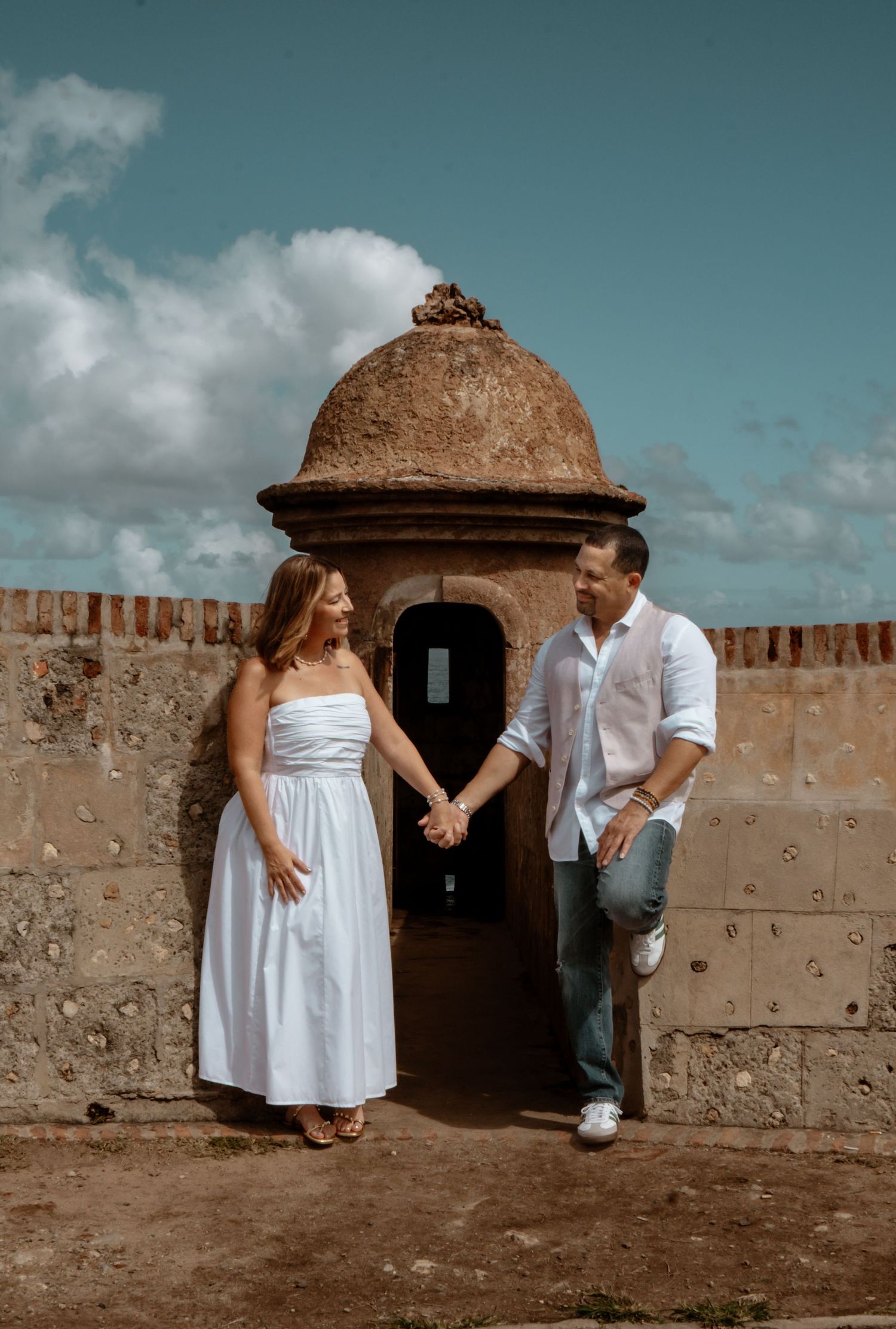Couple posing against historic stone fortress walls under blue skies.