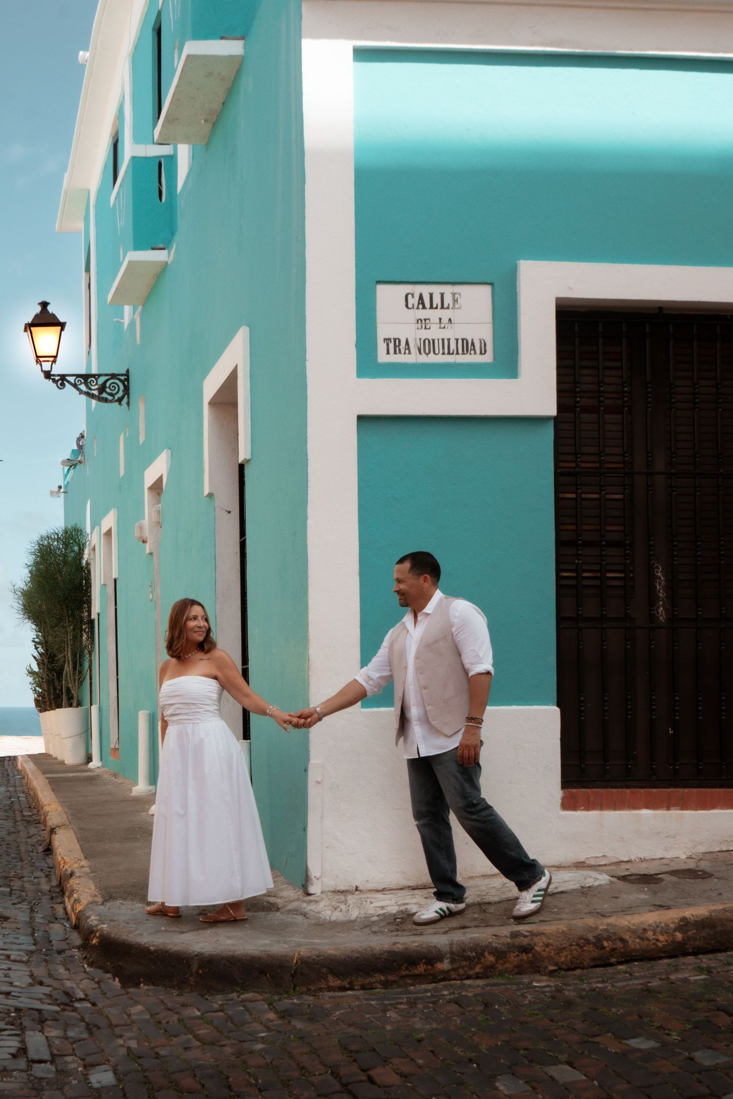 A couple poses playfully along a turquoise colonial street wall in Old San Juan.