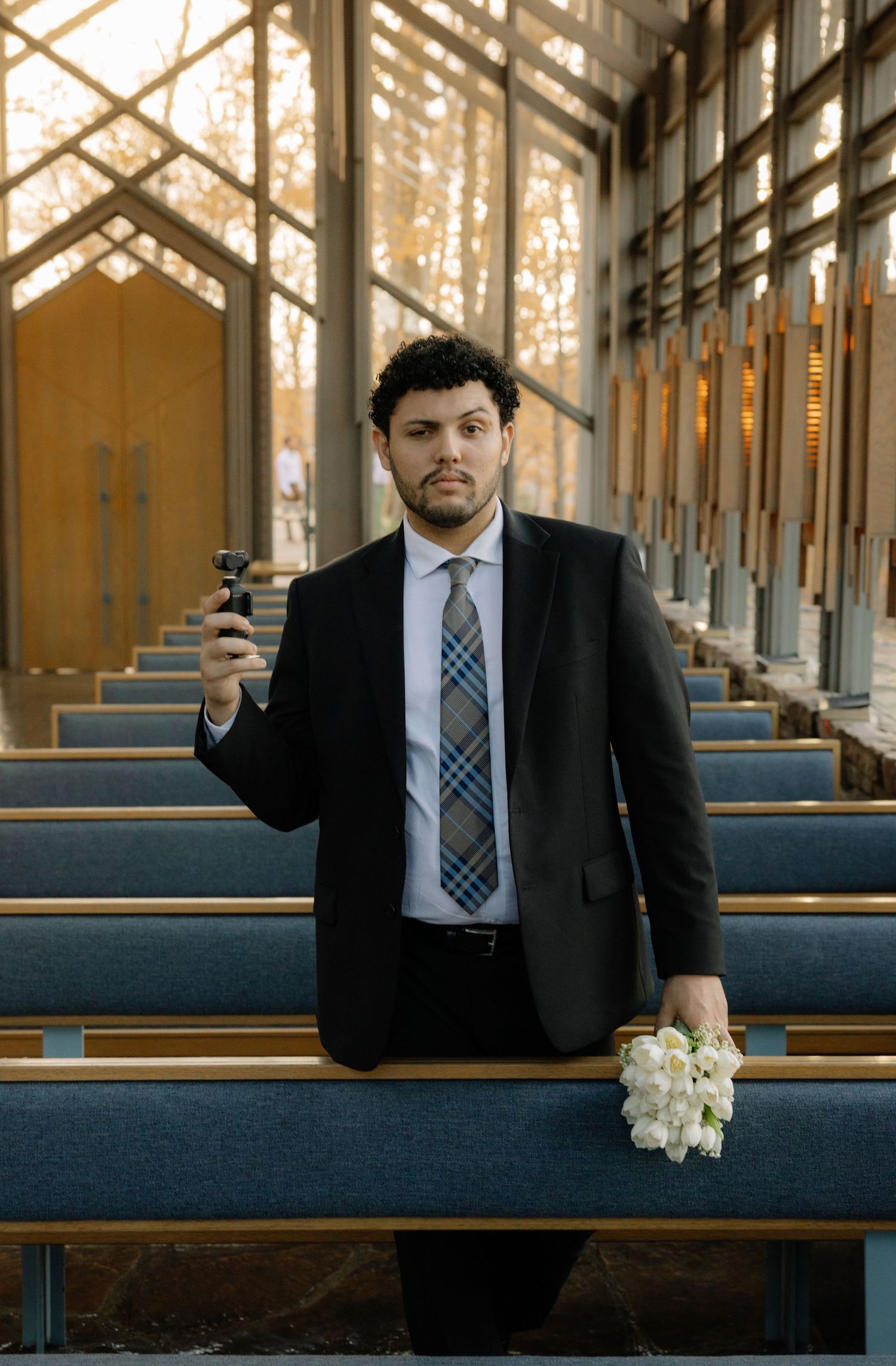 A collage of four photos showing someone in a suit sitting in church pews holding a phone and white flowers.