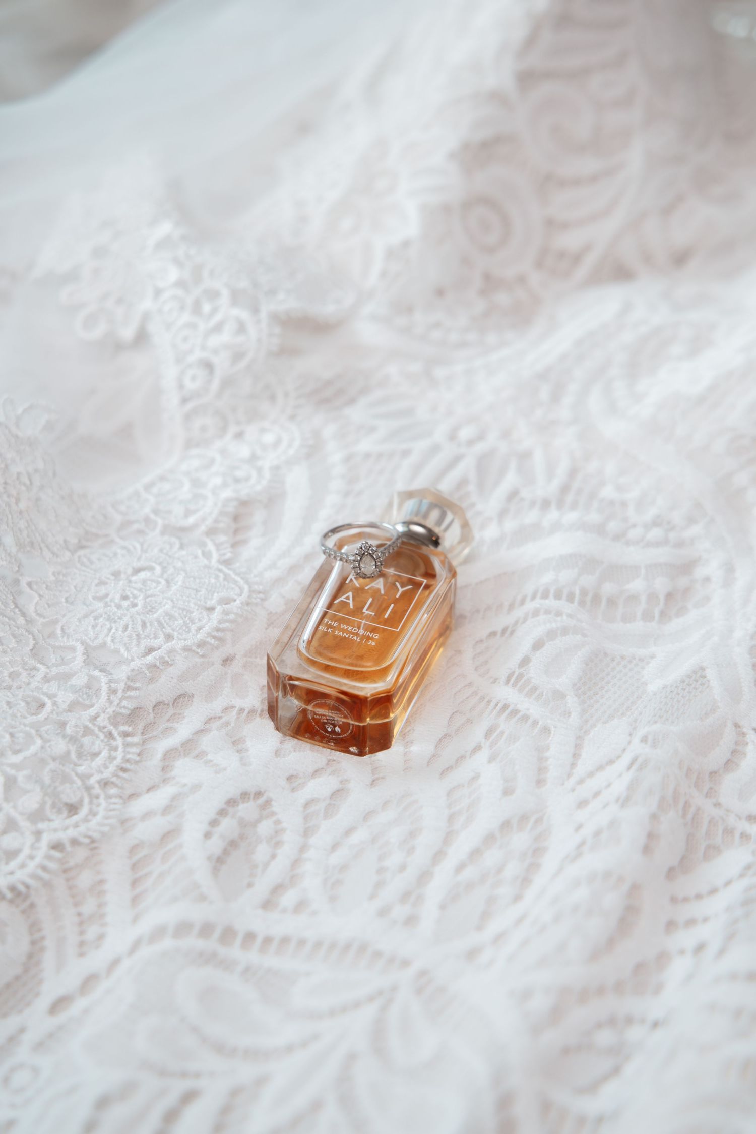 Small perfume bottle sitting on delicate white lace fabric in a romantic composition.