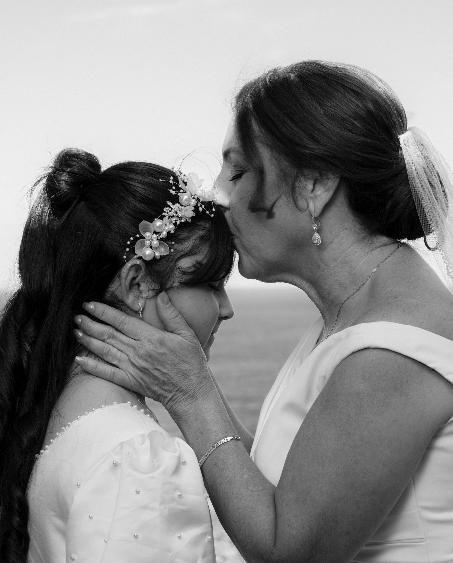 A tender black and white moment captured between two people in formal attire, with a delicate floral headpiece visible.